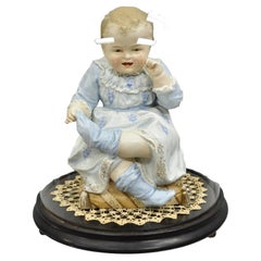 Antica statuetta di bambino seduto in porcellana di bisquit in una cloche circolare di vetro