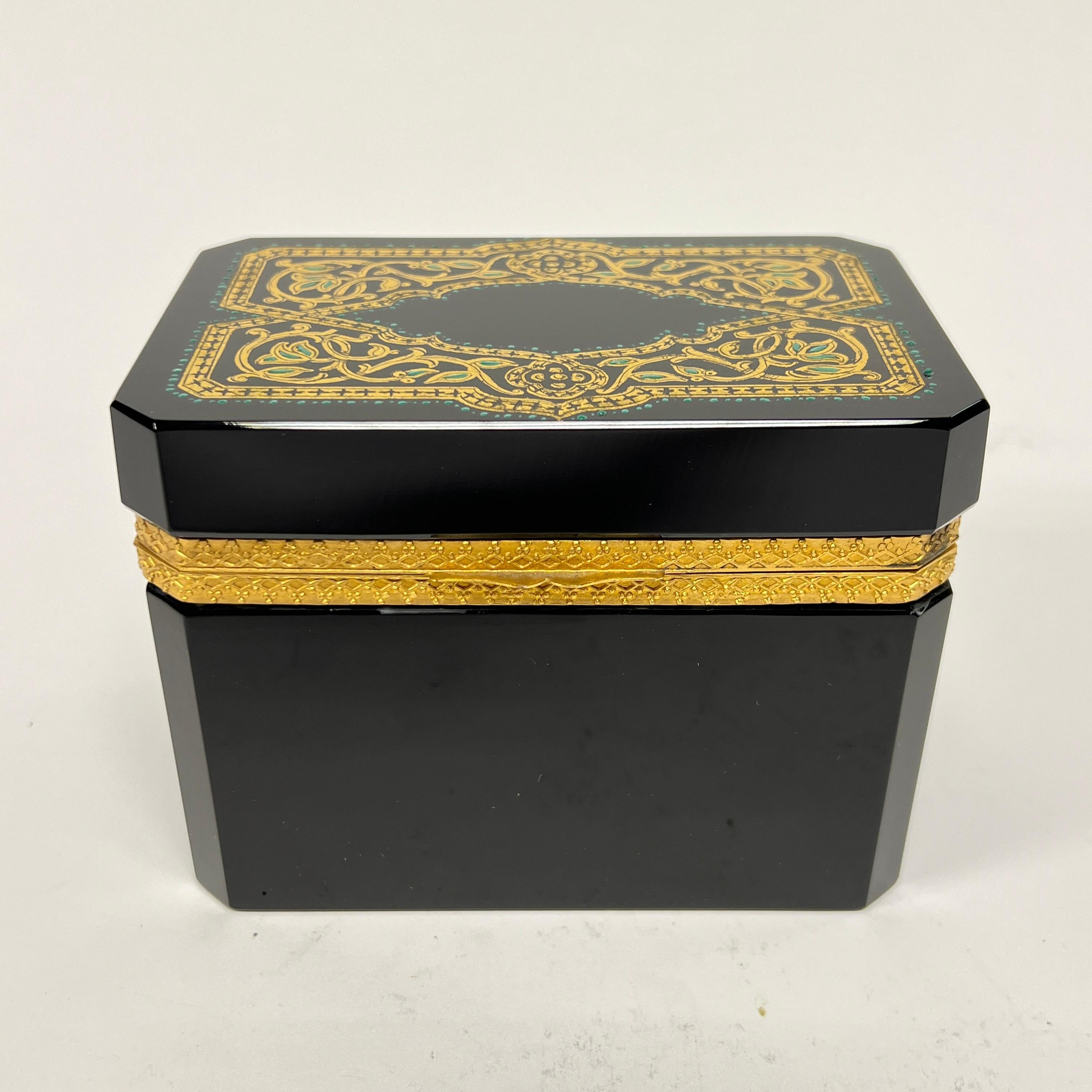 Precioso joyero o caja de baratijas antiguo (de finales del siglo XIX a principios del XX) finamente elaborado en cristal amatista negro con adornos de cuentas de esmalte dorado y turquesa en la tapa, y marco de metal dorado.