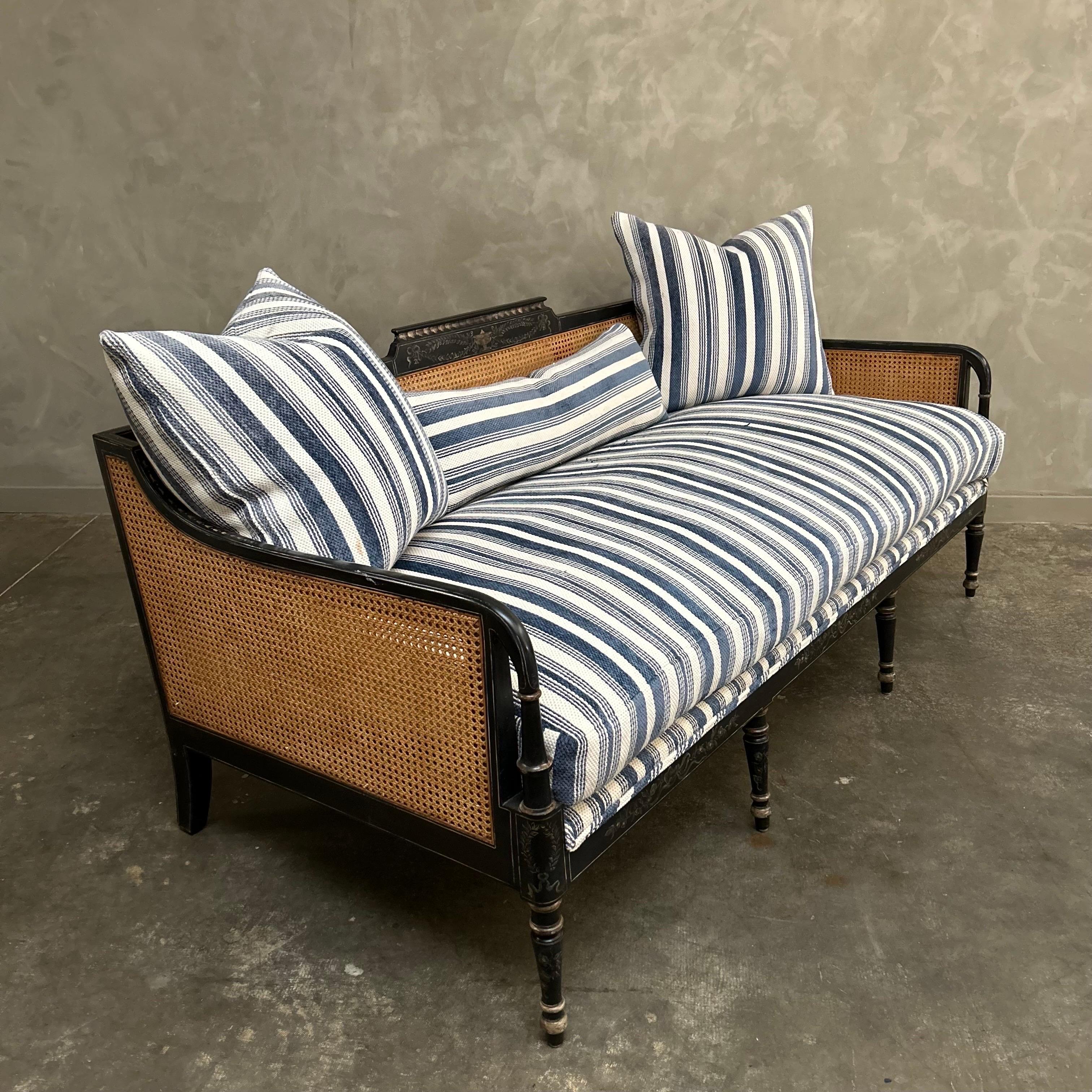 Black Painted cane daybed with hand painted details.
Cane is in good condition with an upholstered decking.
Blue ticking is in good condition, there are some spots of wear, no stains or major issues present. Can be reupholstered in COM or any of our