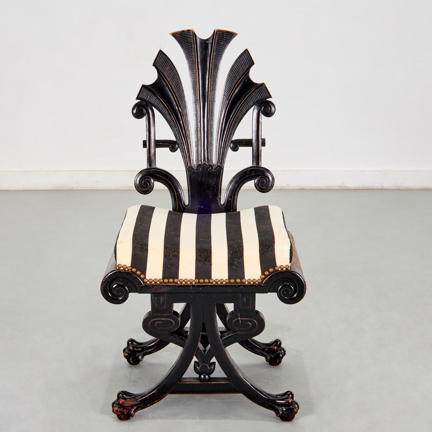 A very striking Antique English Aesthetic Movement black lacquered chair. The chair has an openwork wood back carved as a fan of stylized feathers over a padded seat upholstered in a black and white striped velvet with brass nailhead trim, over