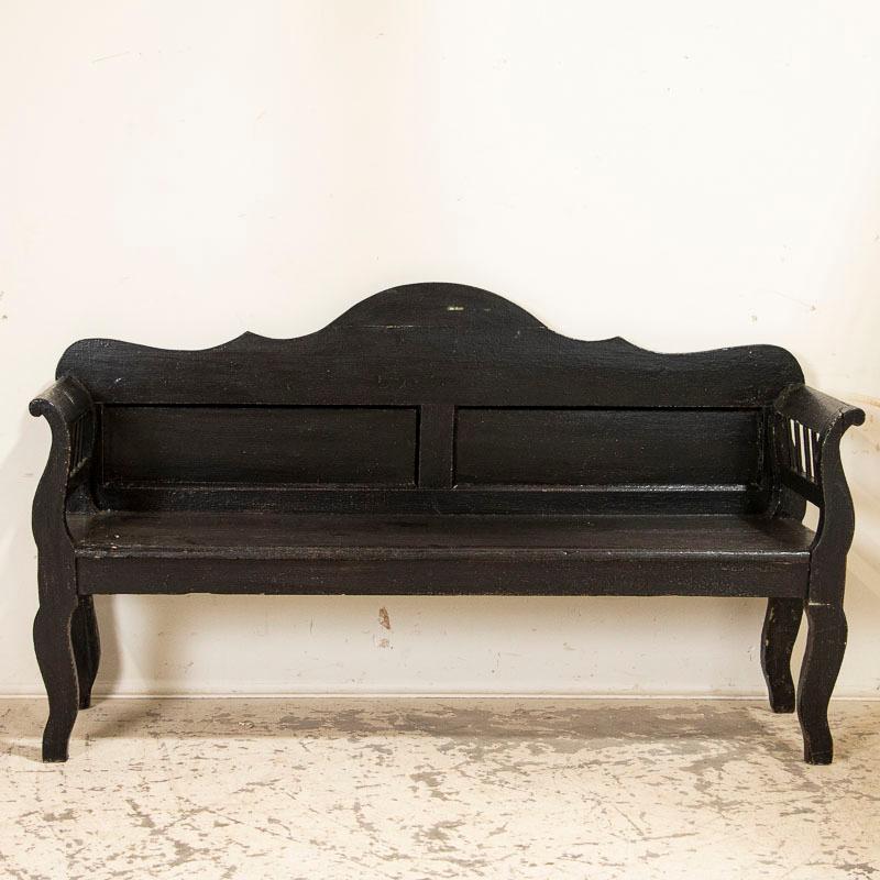 This delightful country bench has a scalloped back accented by curved arms and legs, adding a slight romantic touch to it. The black painted was added at some point in time, which allows it to be used and enjoyed in a variety of ways in today's