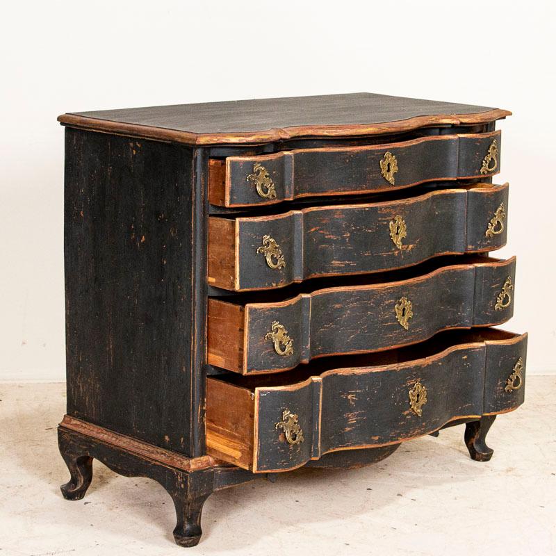 This antique baroque oak chest of drawers from Denmark features a serpentine front, brass hardware pulls and an exceptional matte black painted finish gently distressed to match the age of the dresser. Notice the burnished gold and faint red trim