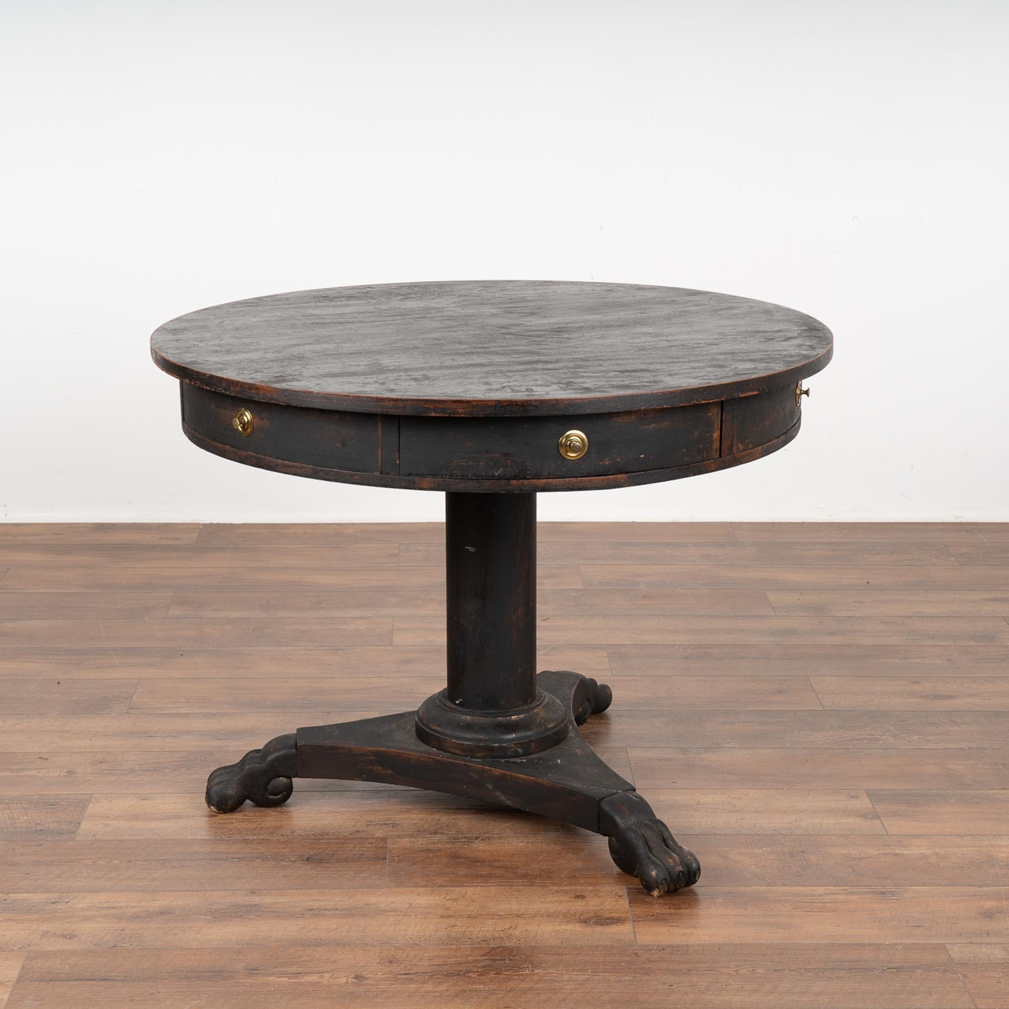 This drum table from Sweden is a special find. It has six drawers and rests on a pedestal base with three heavily carved and dramatic feet.
Later painted black, the slight distressing simple adds aged grace to this lovely occasional table.