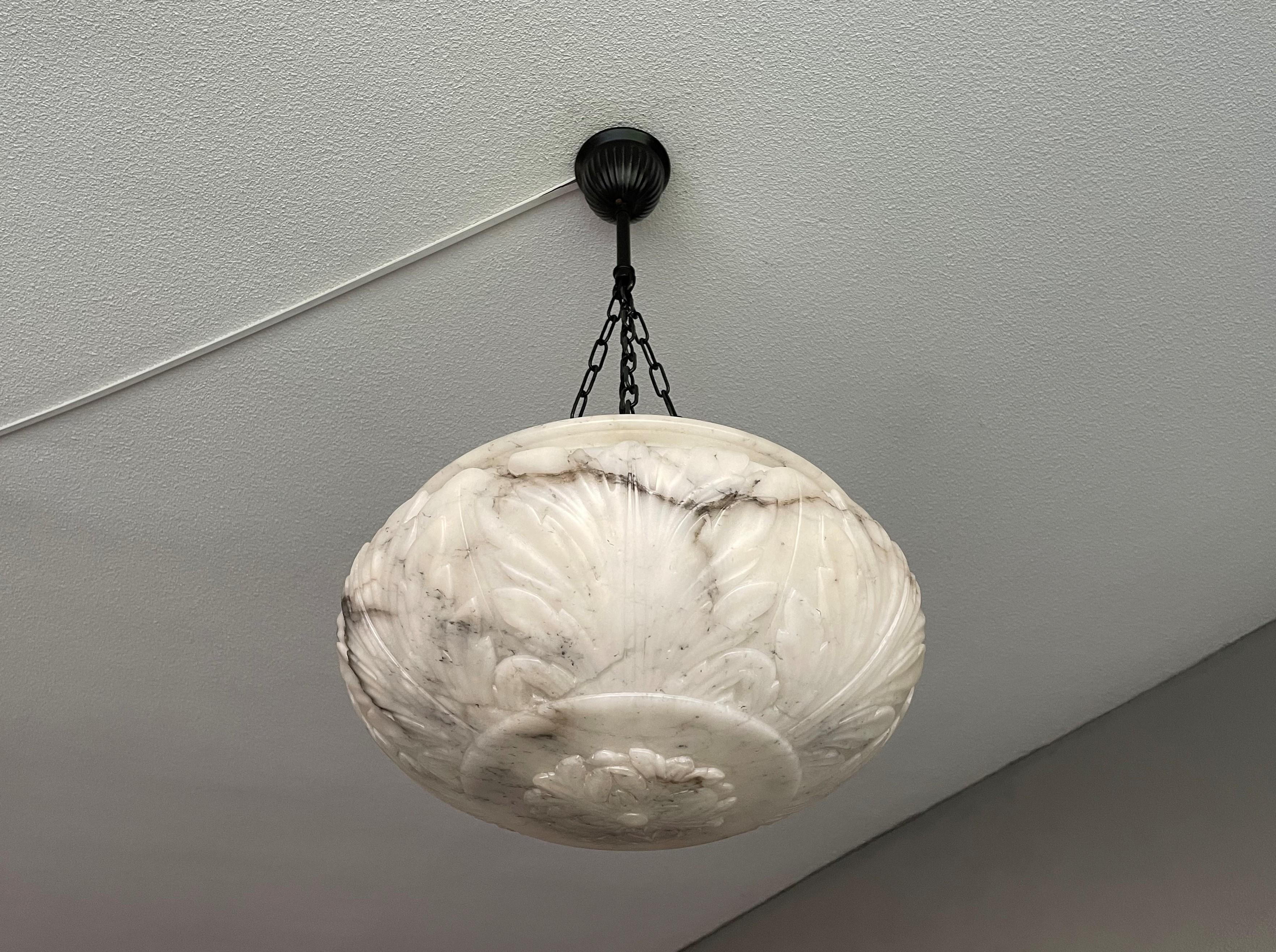 Top class light fixture with a stunning alabaster shade and a blackened chain & canopy.

Thanks to its unique design and good size this hand carved antique alabaster chandelier will light up both your days and evenings. The stunning and deep shade