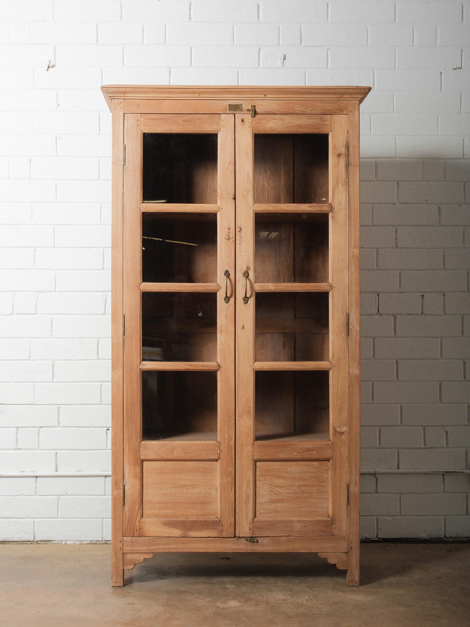 Dieser wunderschöne antike Schrank aus gebleichtem Teakholz weist eine warme, natürlich verwitterte Oberfläche auf, die die organische Bewegung und Maserung des Holzes hervorhebt. Dieser handgefertigte Schrank mit doppelten Glastüren bietet