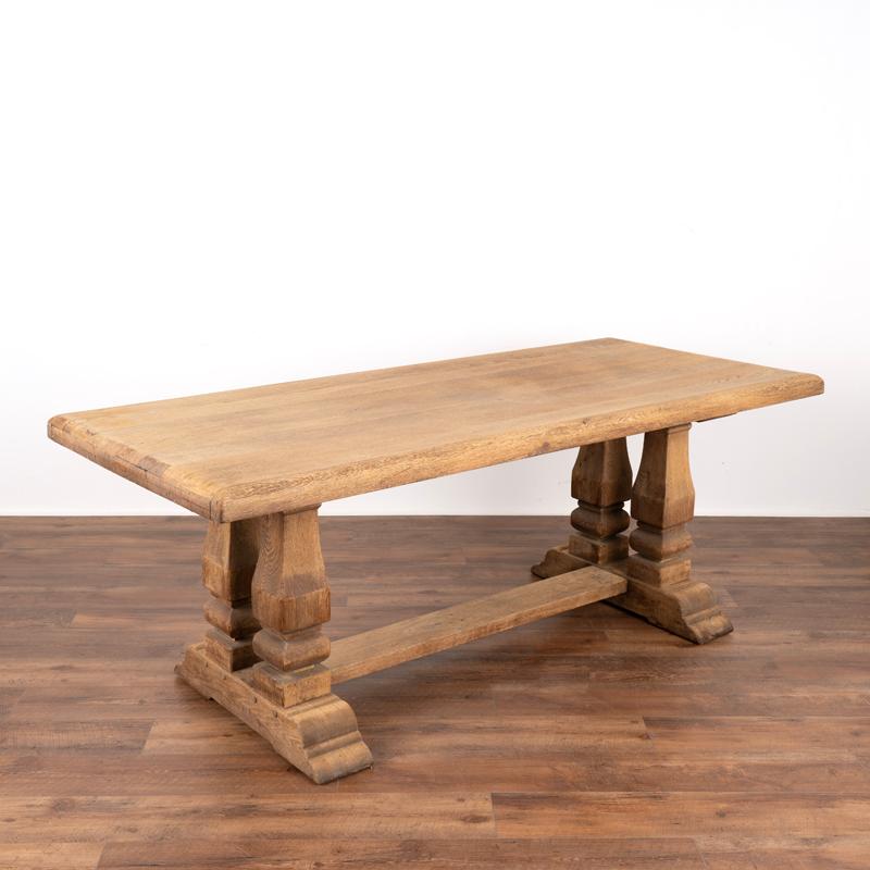 This bleached oak table has commanding presence thanks to the heavy carved columns that create the visually stunning four legs of the large trestle base. The thick top invites one to touch it. This dramatic 6.5' long table will make an impressive