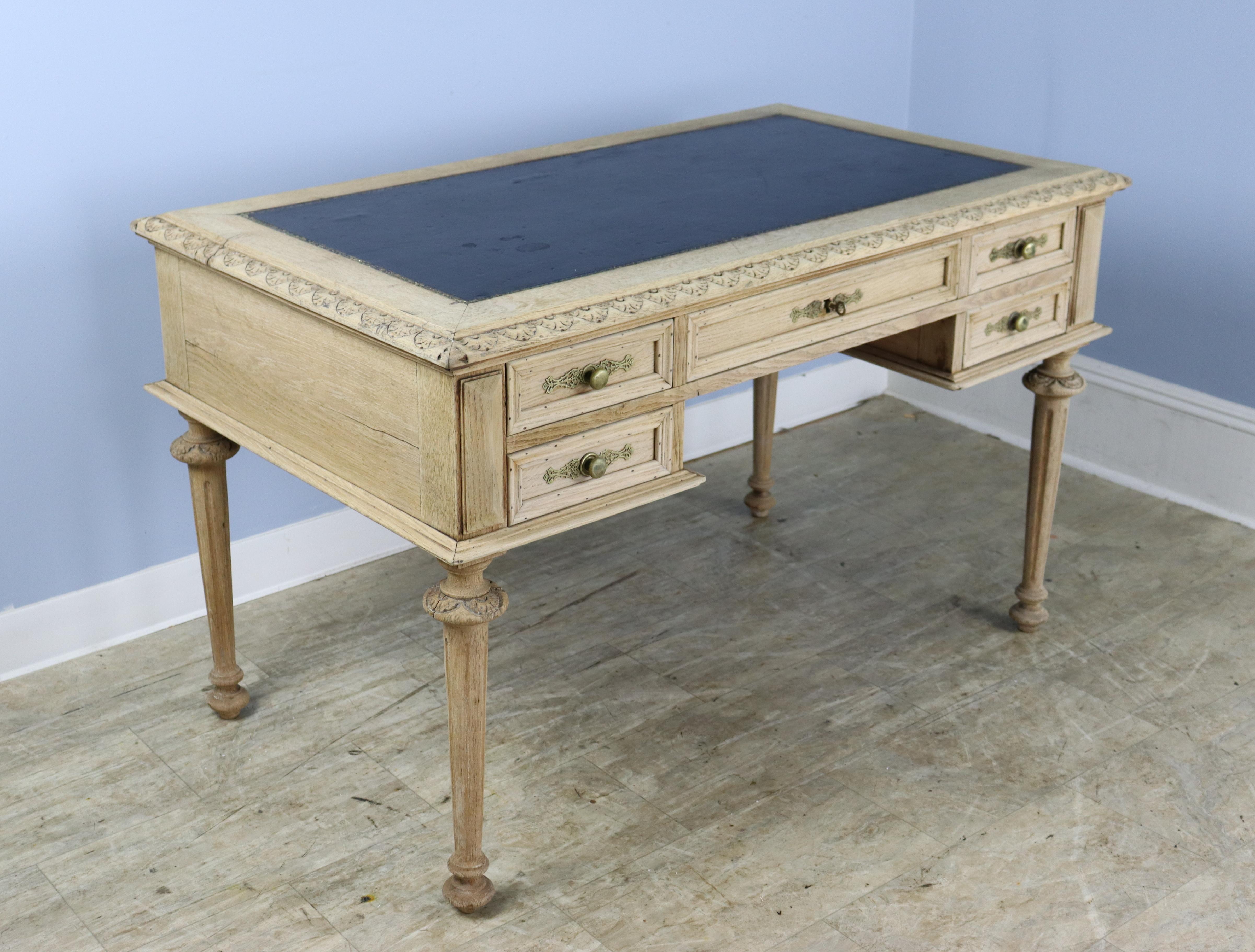 An intricately carved oak desk, bleached for a fresh modern look. The leather is in good condition, with small areas of wear, shown in thumbnails. The are two deep drawers on either side , and a wide center drawer. The key shown does not lock the