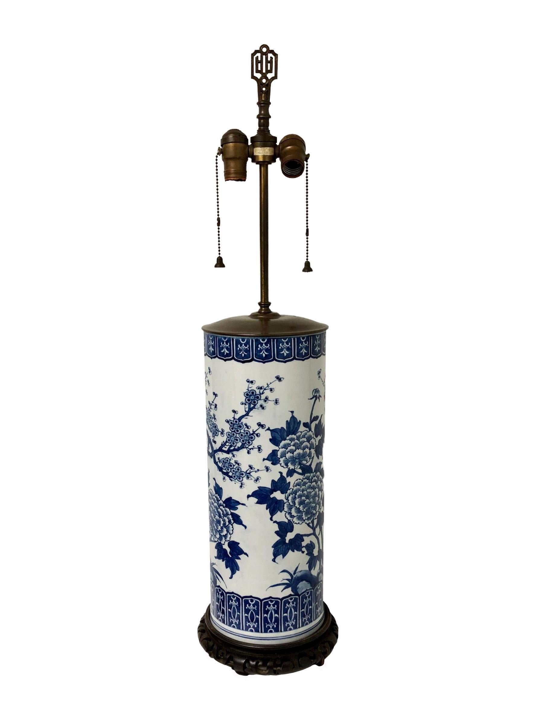 A 19th century blue and white porcelain vase as a lamp. Lamp is most likely Japanese but can’t see the bottom because of the attached Chinese carved wooden base. Original finial with two sockets and pull chains have little bells at the end of them. 