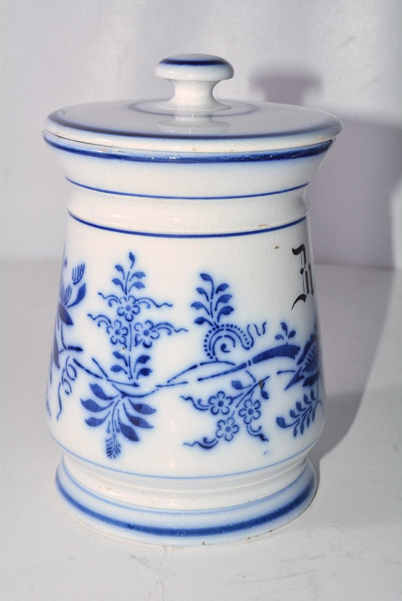 The antique German lidded flow blue pottery canister has blue flowers and leaves on a white background. The label reads Zucker or German for sugar. Other similar canisters available.