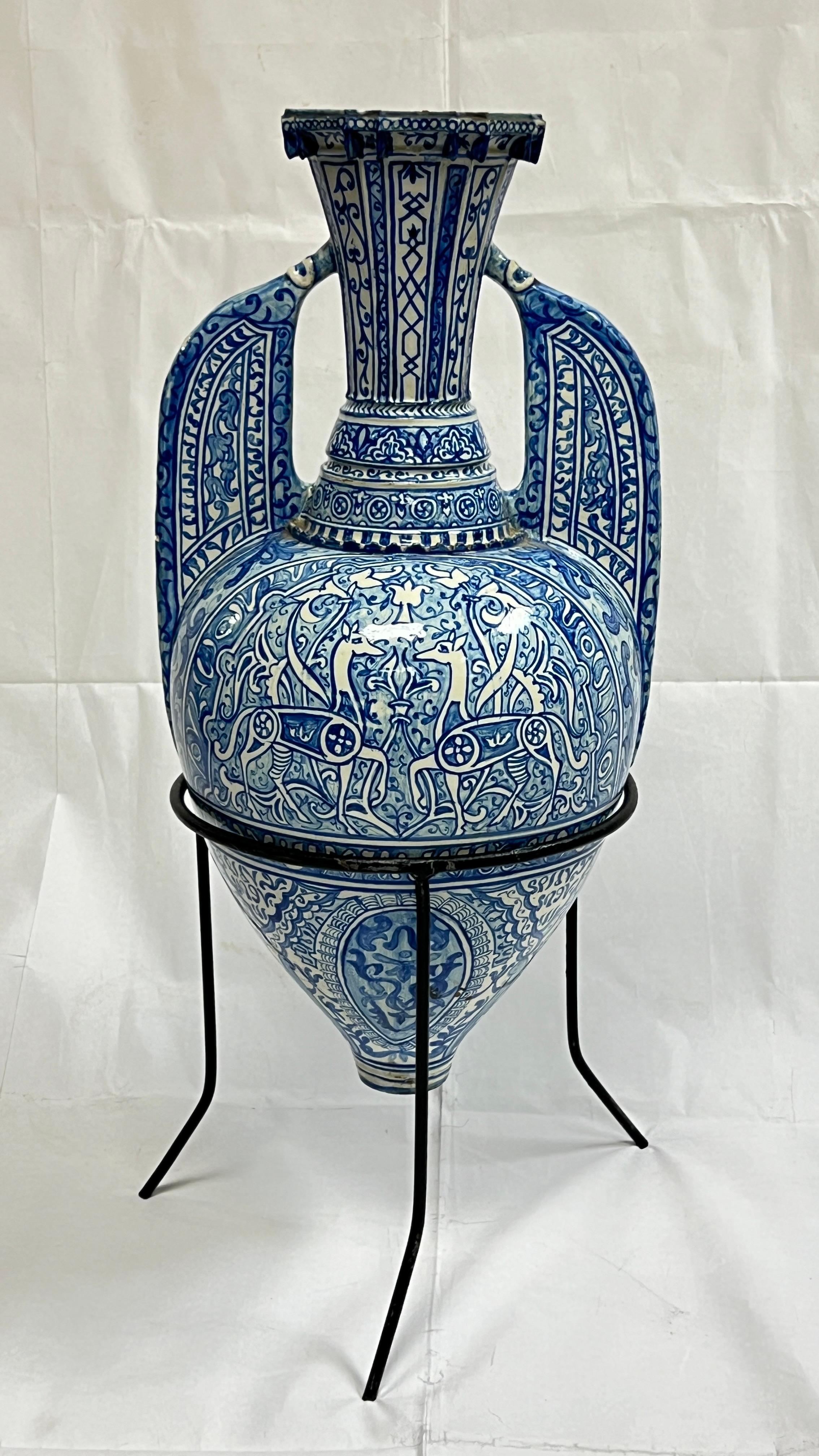 Antique 19th century Hispano-Moresque tin-glazed earthenware amphora vase with hand-painted cobalt blue designs of deer and flowers, with later iron stand.  Vase 21 inches tall and 25.5 inches mounted on stand.