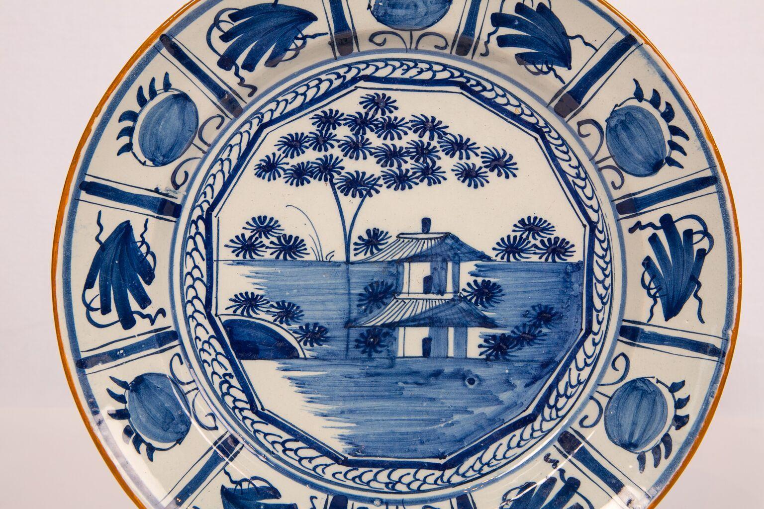 We are pleased to offer this Antique blue and white Delft charger with a well-painted landscape showing a house and trees. The decoration is crisp. The scene is framed by an attractive double border and completed with a slip-decorated orange/brown
