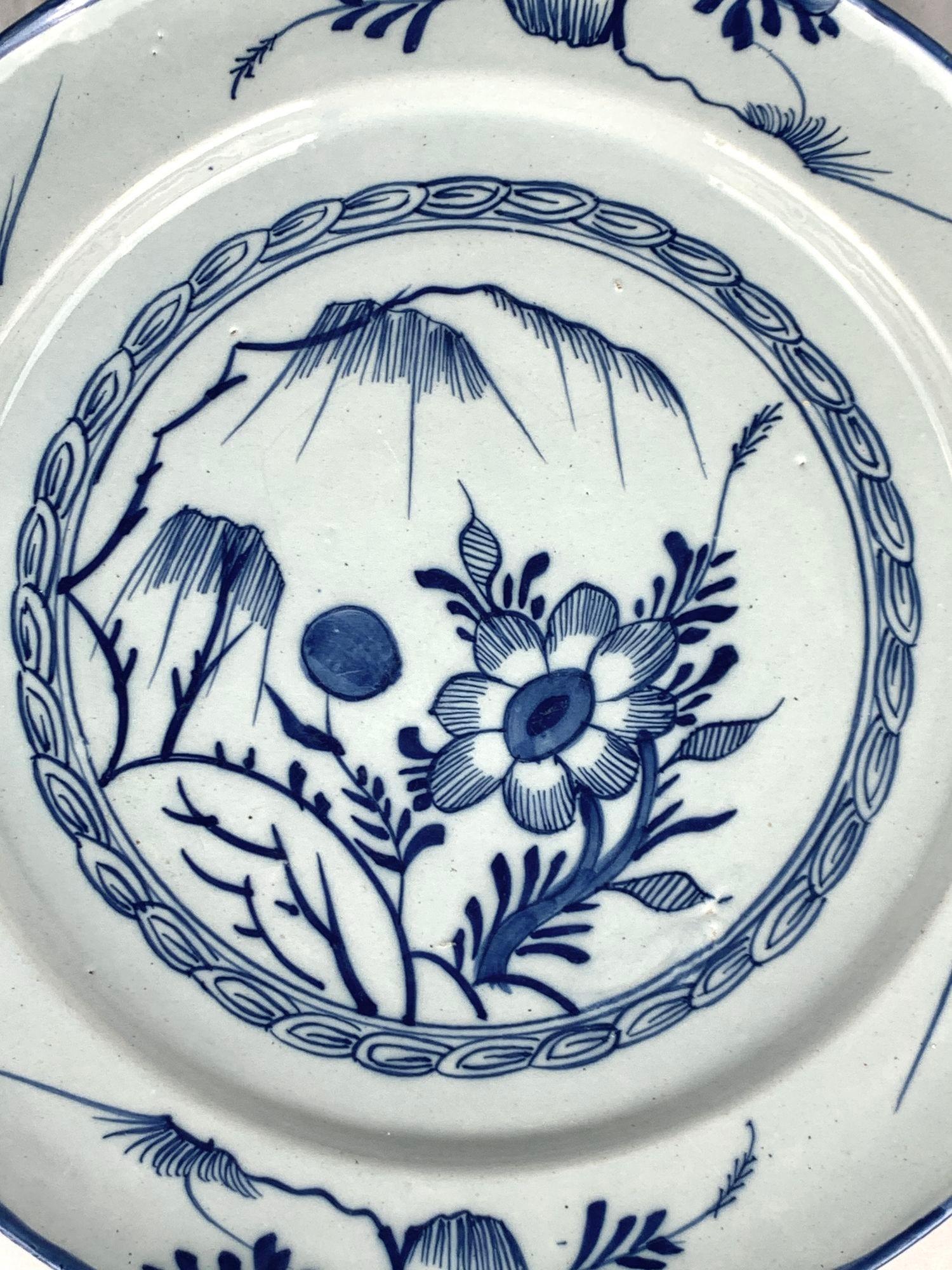 Questo grazioso caricatore di Delft è stato dipinto a mano in Inghilterra a metà del XVIII secolo, intorno al 1765.
Il centro mostra una scena ingenua di giardino con un salice, un fiore di grandi dimensioni e un grande bocciolo blu.
La decorazione