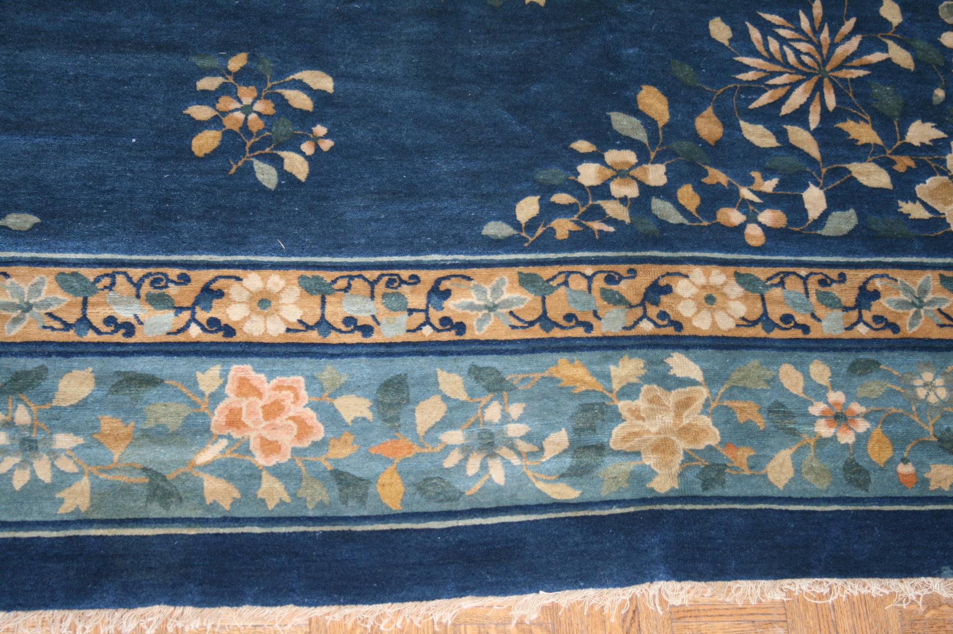 This room size antique was woven in China toward the end of the 19th century. It features a traditionally Chinese design with a central medallion containing a floral motif on a navy field. Outside of the medallion the field is sparsely populated by