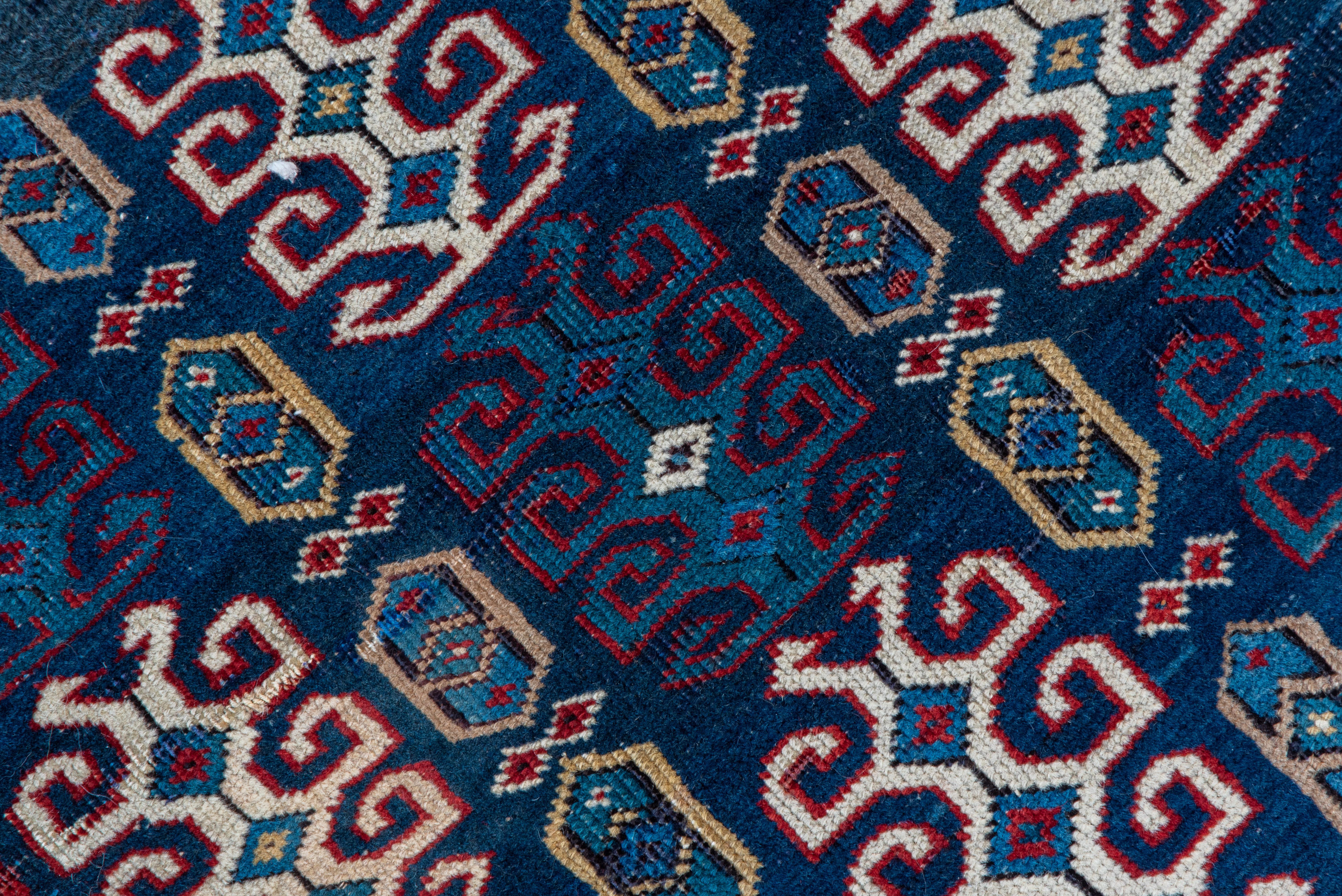 Cet éparpillement de village du nord-est du Caucase montre des colonnes d'éléments crochus et des octogones plus petits sur le sol marin. Bordure principale ivoire avec le motif classique du calice caucasien et de la feuille inclinée, et bordures