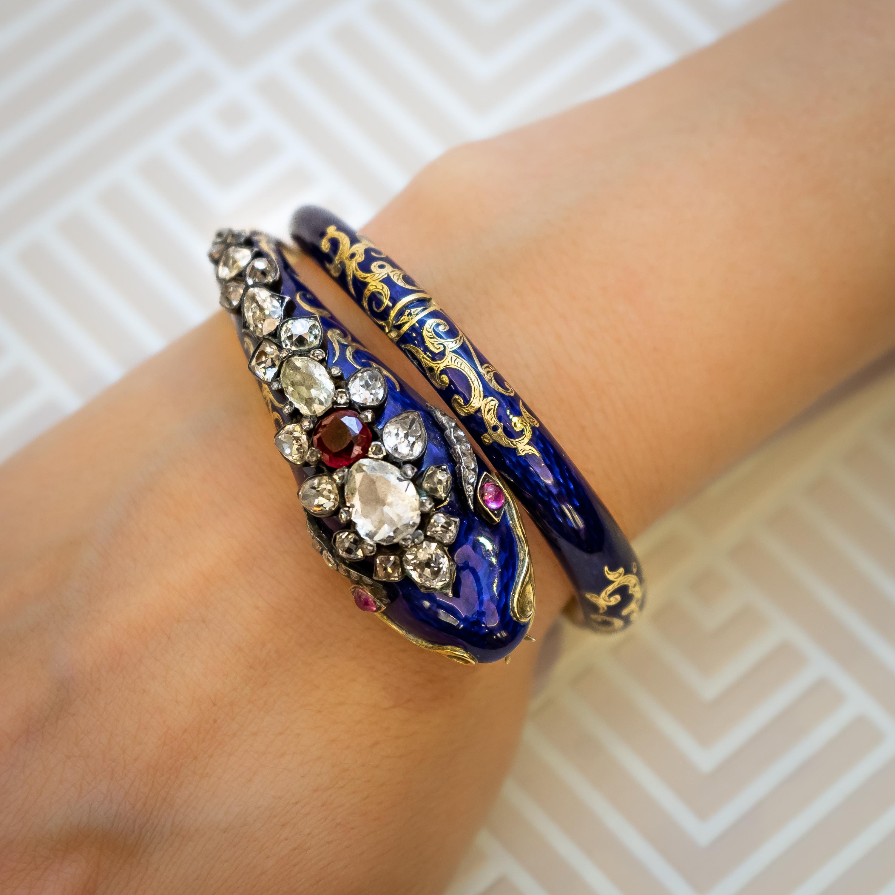 An antique snake bangle, with blue enamel on gold, with gold engravings either side of the four hinges. The head is set with old-cut and rose-cut diamonds, with a total weight of approximately 5.50ct, cabochon ruby eyes and a red garnet topped