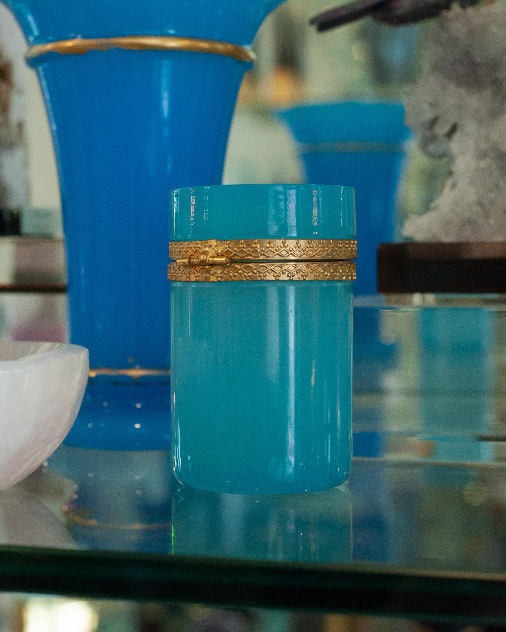 Cette exquise jarre ou boîte en opaline bleue est une pièce étonnante, dotée d'un couvercle monté en bronze doré méticuleusement travaillé qui ajoute une touche supplémentaire d'élégance et de sophistication. Le verre opalin a été principalement