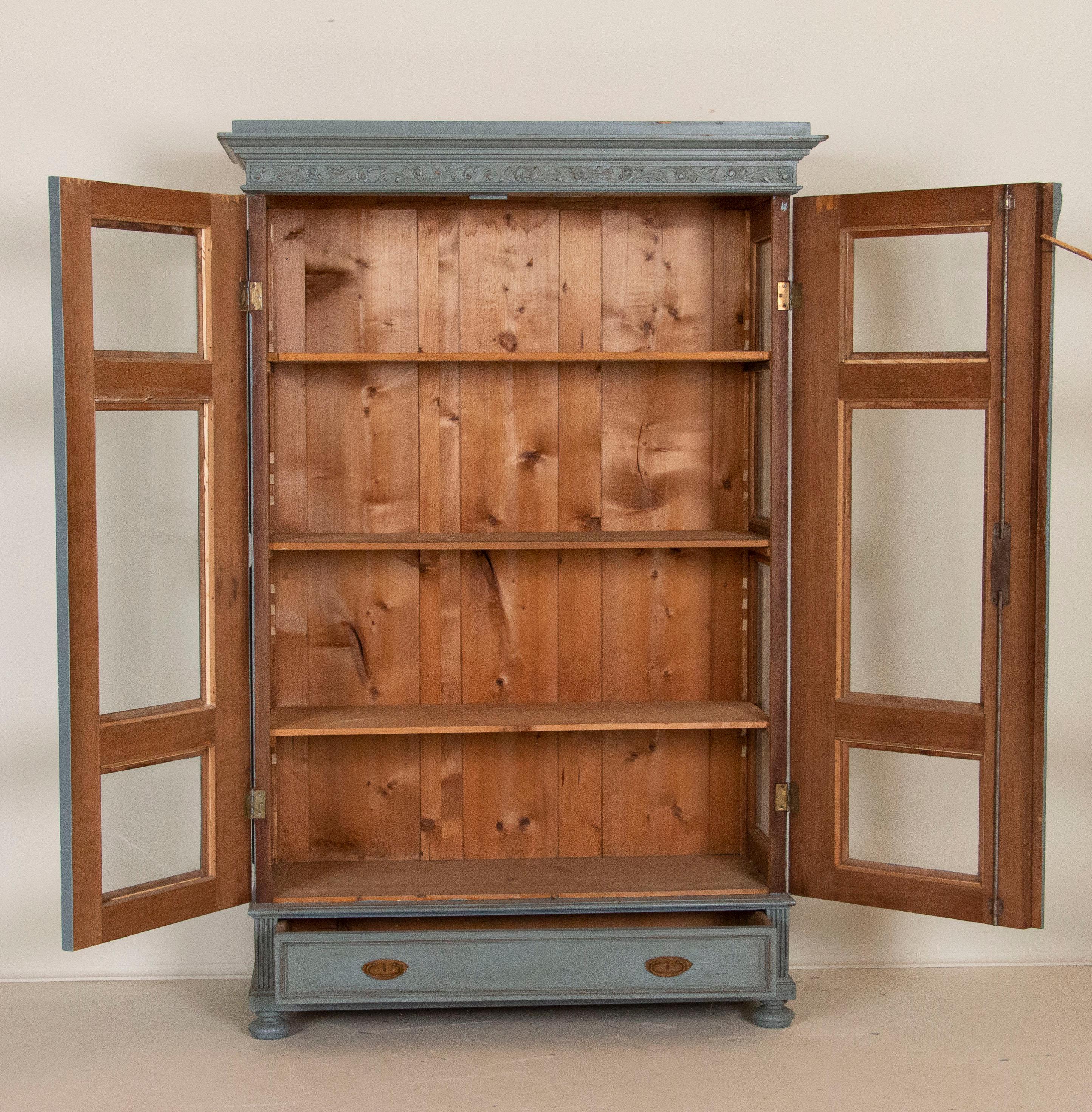 The glass panels in the front doors are continued along the sides as well, making this bookcase an ideal display cabinet for china or other collectibles. The soft blue paint is lightly distressed along the carved details and panels, adding character