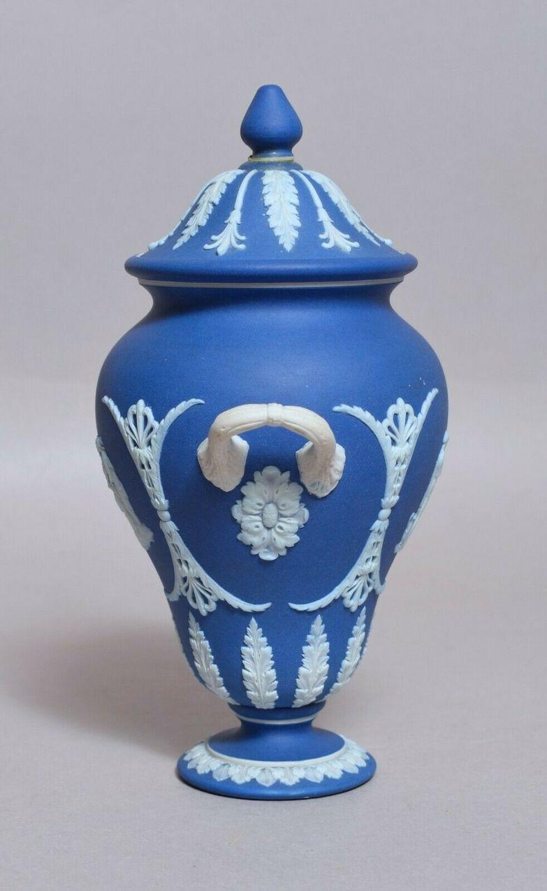 An attractive example of an English Jasperware Wedgwood urn of medium size proportions, late 19th century.

The twin handle ovoid form urn decorated in relief depicting neoclassical scenes flanked by leafy swags on white on a dark blue ground. The