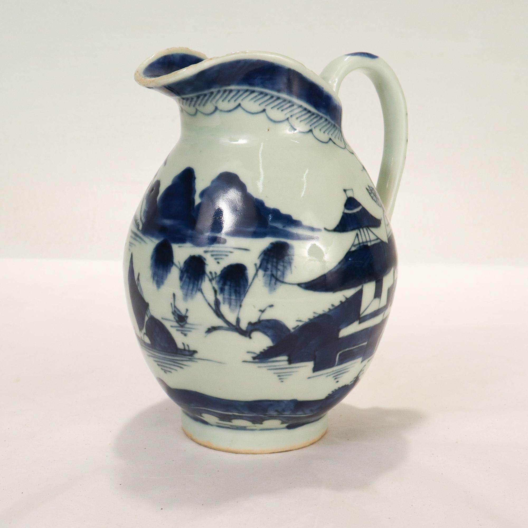 A fine Canton Chinese Export porcelain pitcher.

Decorated with blue underglaze throughout depicting a Chinese village near the water, with a boat and foliage.

The handle is decorated with a flower, and the pitcher's rim has a blue border on