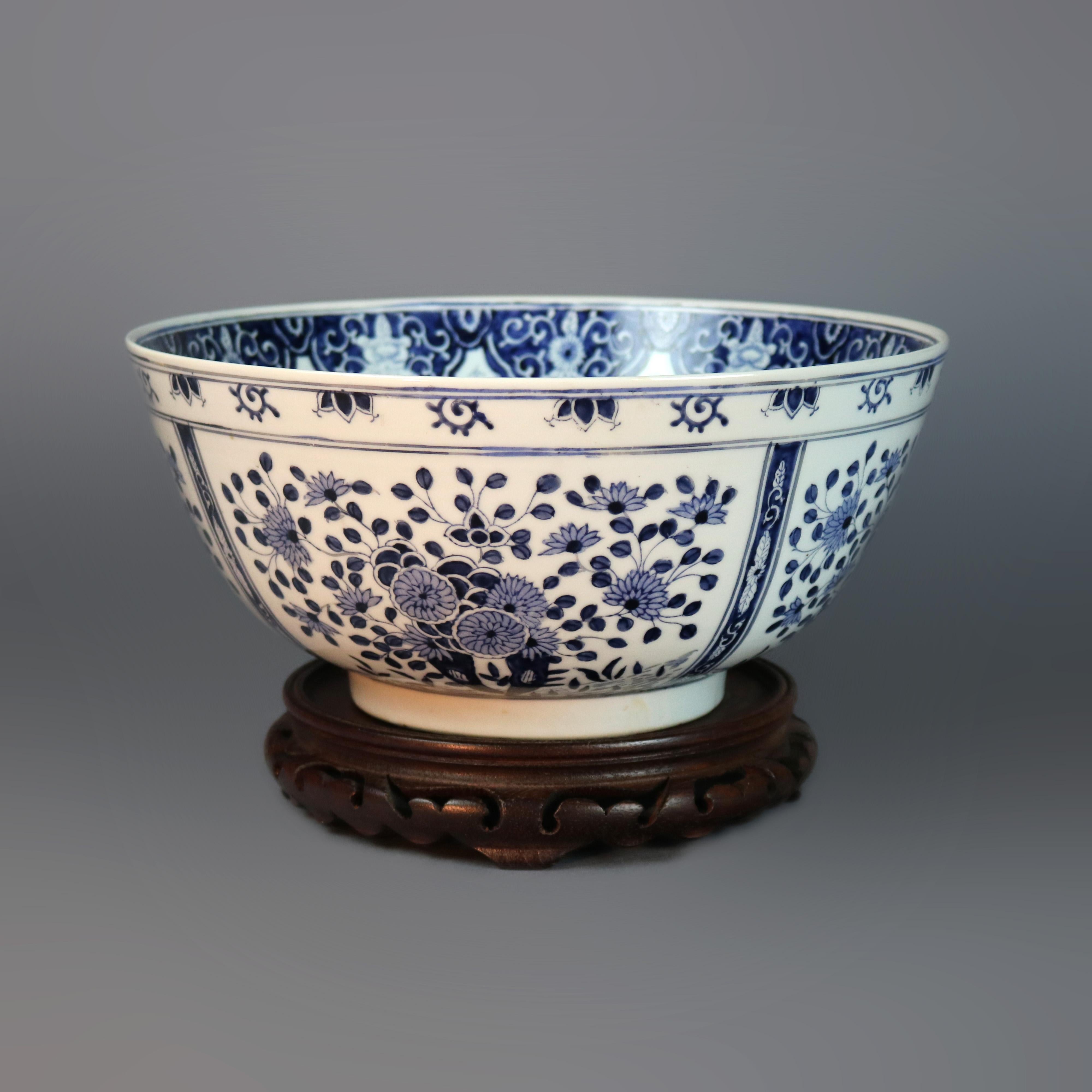 An antique blue and white Japanese porcelain bowl offers all-over stylized floral decoration and is seated on carved hardwood base, stamp reads 