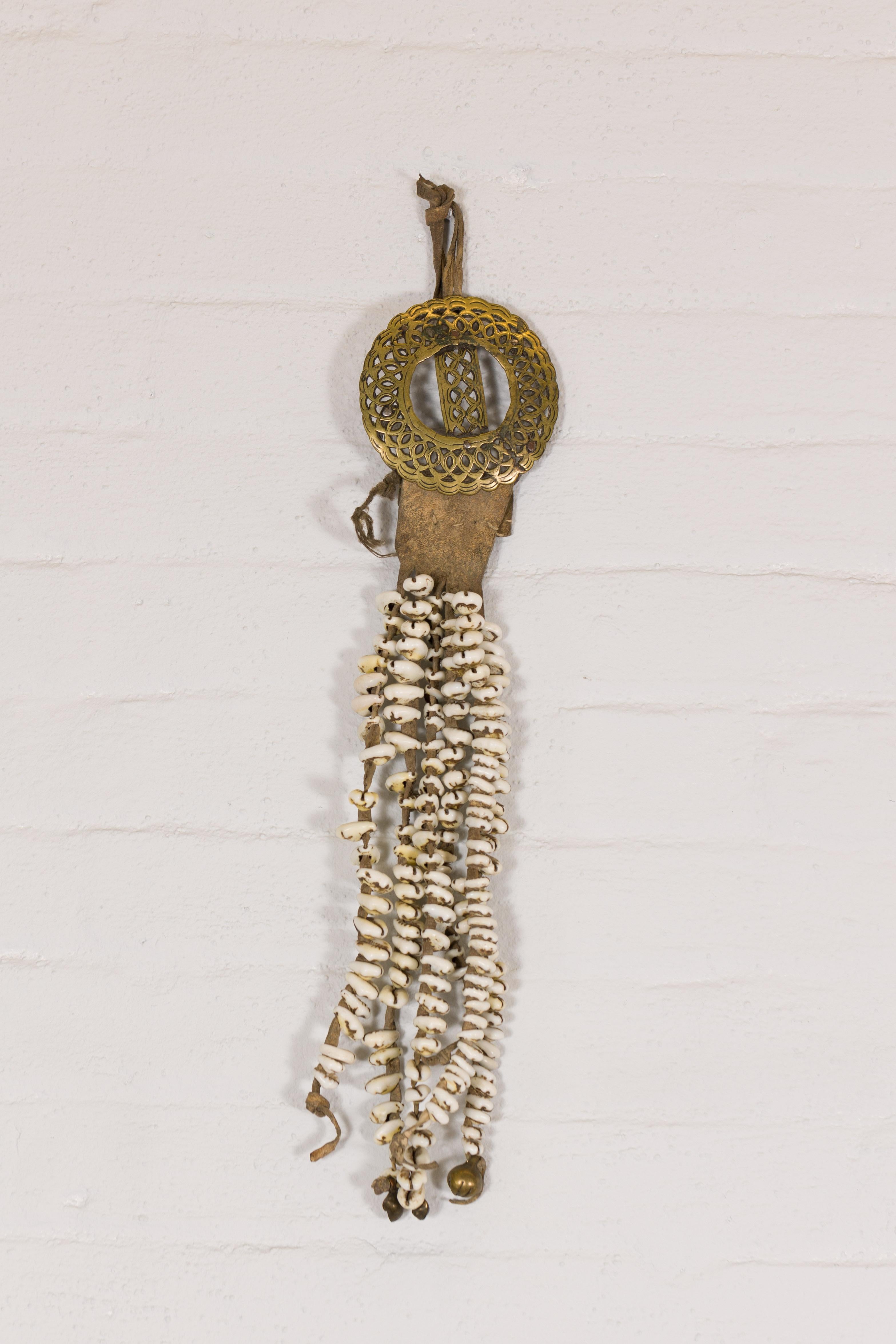 An antique body ornament from India, Nepal or Tibet, made of strands of old Himalayan shells secured to a brass circular buckle with pierced motifs. Embark on a cultural odyssey with this antique body ornament hailing from the mystic terrains of