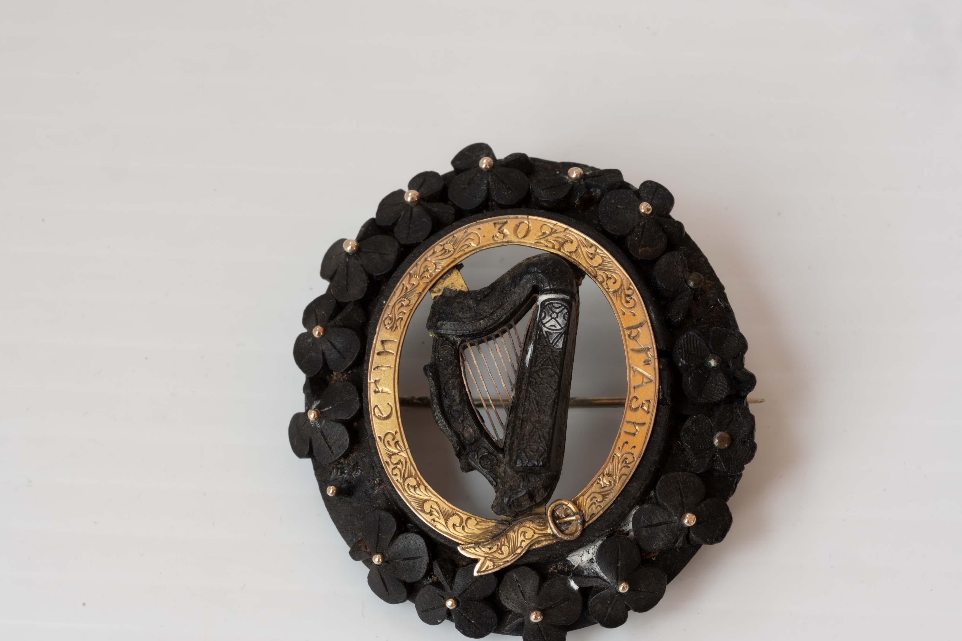 Antique Bog oak Irish harp pin brooch, Ireland Forever motto, Erin Go Bragh. With a carved design and clover leaves with gold-tone dots and rolled gold on metal. Central harp design, the brooch measures 2 1/4 inches x 2 inches (5.5 cm x 5 cm). The