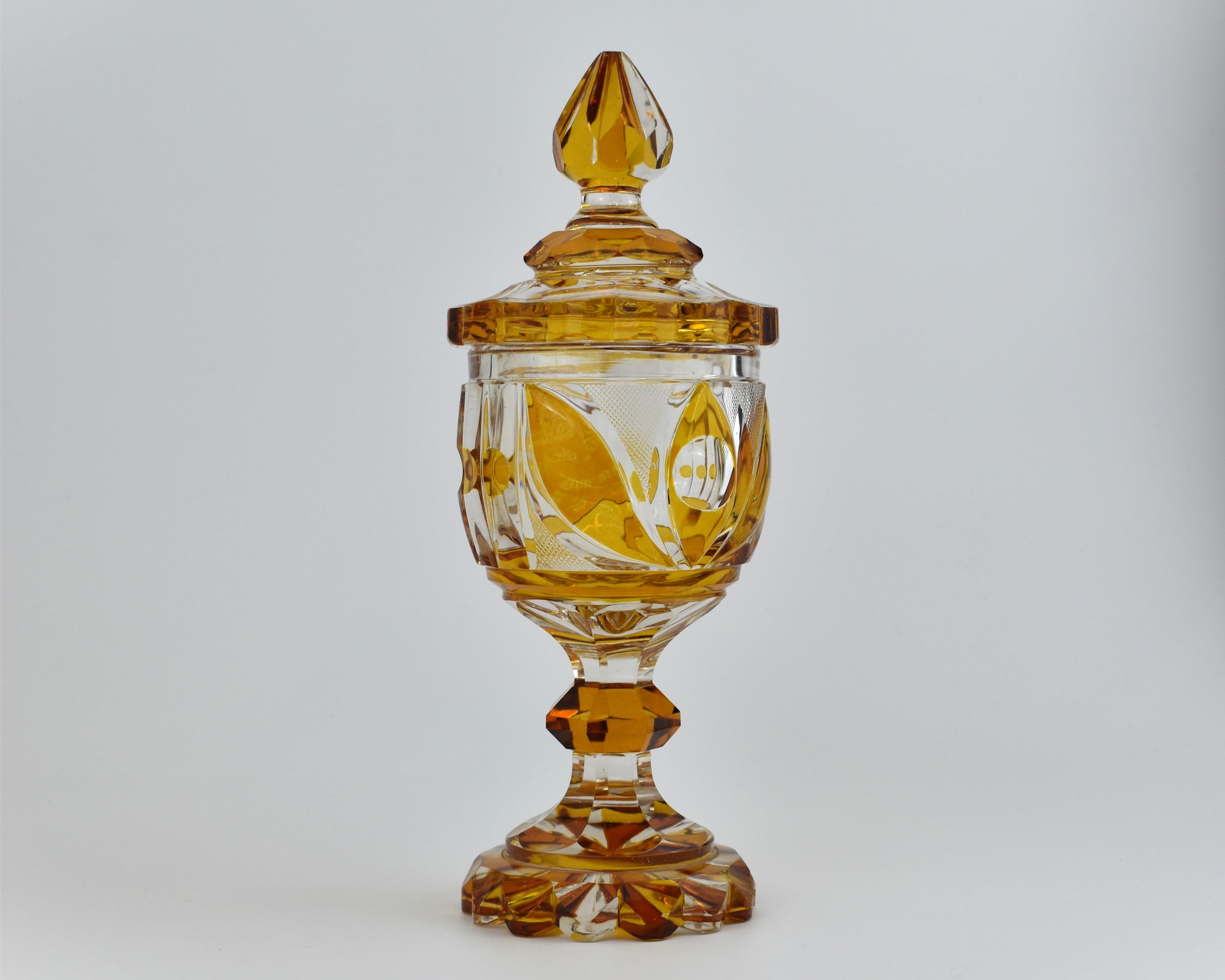 Calice colorato d'ambra del XIX secolo, il corpo a forma di coppa con un pannello circolare rialzato, tagliato in molteplici forme e motivi, inciso con un'iscrizione,   poggia su un piede smerlato in vetro tagliato con una base svasata nella parte