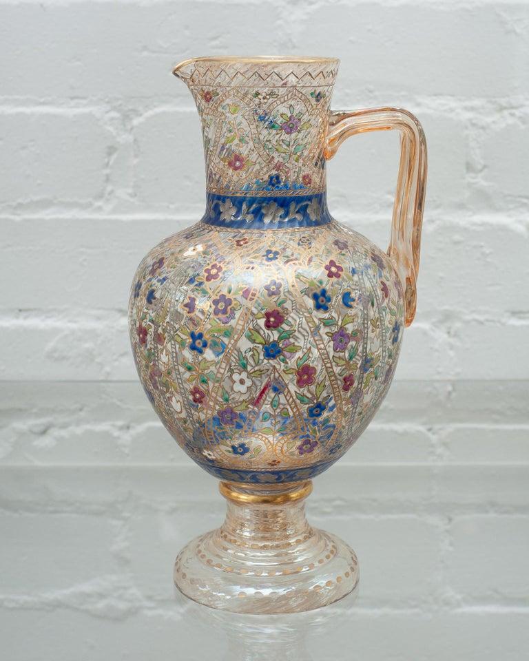 Esta preciosa jarra de agua de cristal de Bohemia, de hacia 1920, es una auténtica obra de arte, con un exquisito trabajo de esmalte y un delicado dorado. La jarra está adornada con motivos florales bellamente pintados en colores vivos y atrevidos,