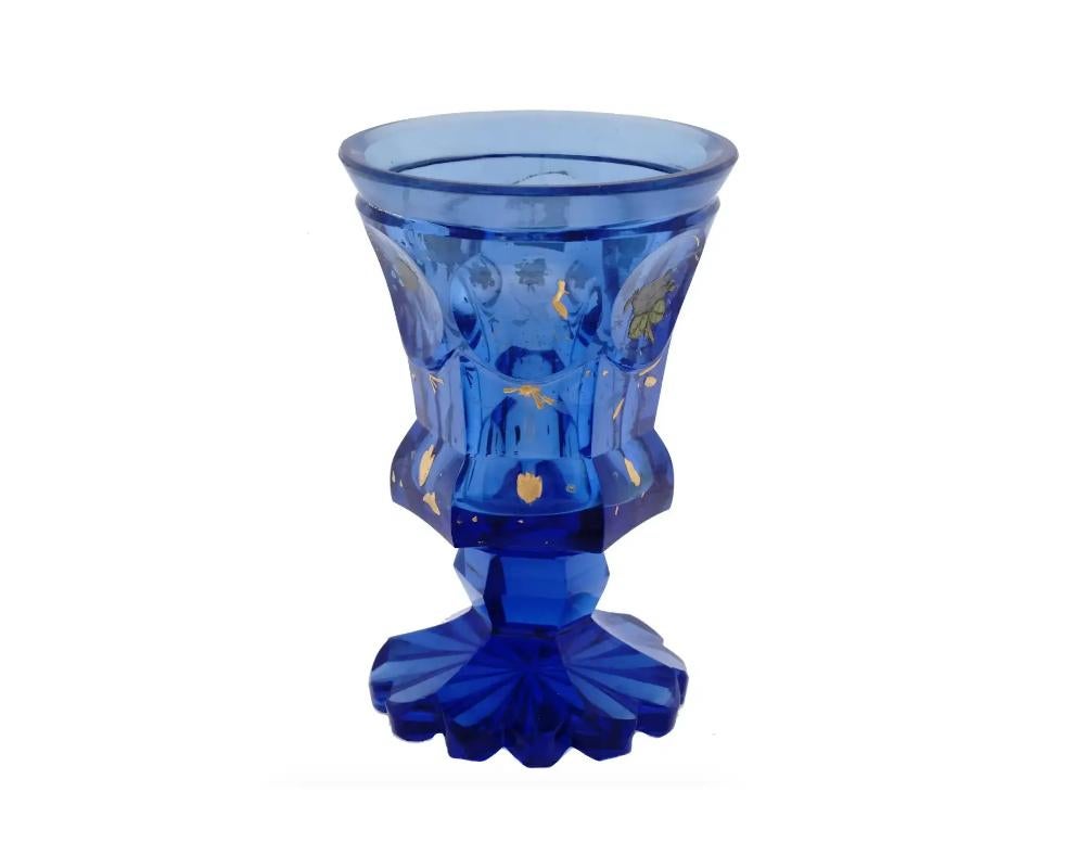 An antique European, probably Czech, footed sapphire blue Bohemian glass goblet or tumbler. The ware is made in a cut glass and indented type panels design. The exterior of the decanter is adorned with overlays made in floral and berries designs,