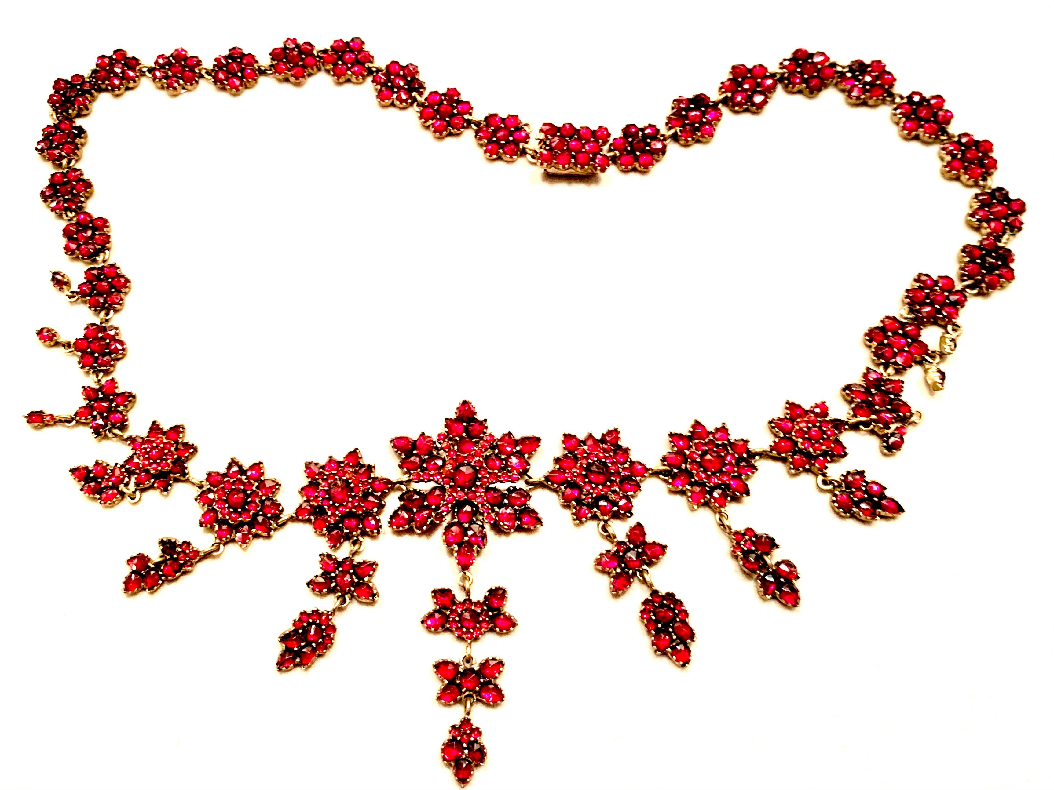 This fine garnet necklace is designed as a series of garnet flowers and stars. The three flowers in the center feature dangling butterflies and leaves. Seven elements  in the front of the necklace have two layers of flowers. The garnets of