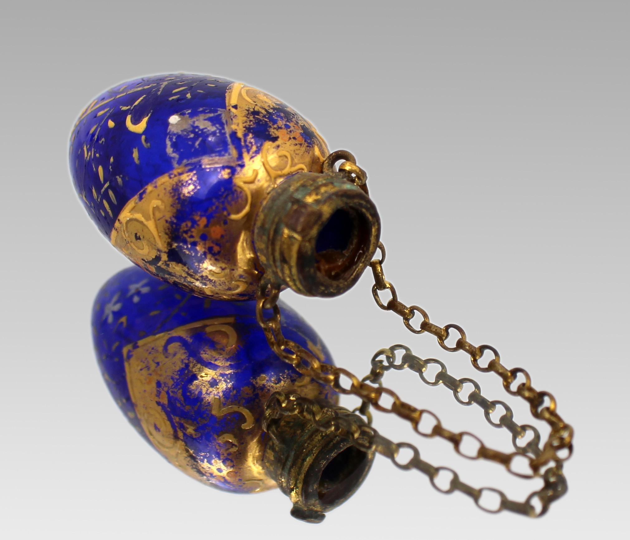 Antique Bohemian Gilt and Enamelled Blue Glass Chatelaine Scent Bottle, circa 1870

A finely decorated 19th-century Bohemian scent bottle, crafted in deep cobalt blue glass and adorned with hand-applied gilt foliate scrolls and delicate white enamel