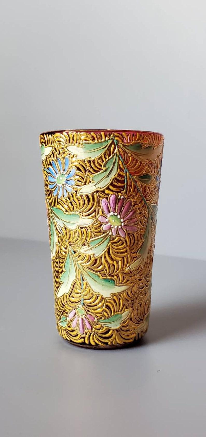 Un petit verre d'art décadent de Bohème, émaillé et doré, de couleur rouge canneberge. 

Fabriqué à la main en Bohemia (aujourd'hui République tchèque) au tournant de la fin du XIXe siècle et du début du XXe siècle, ce magnifique verre d'art