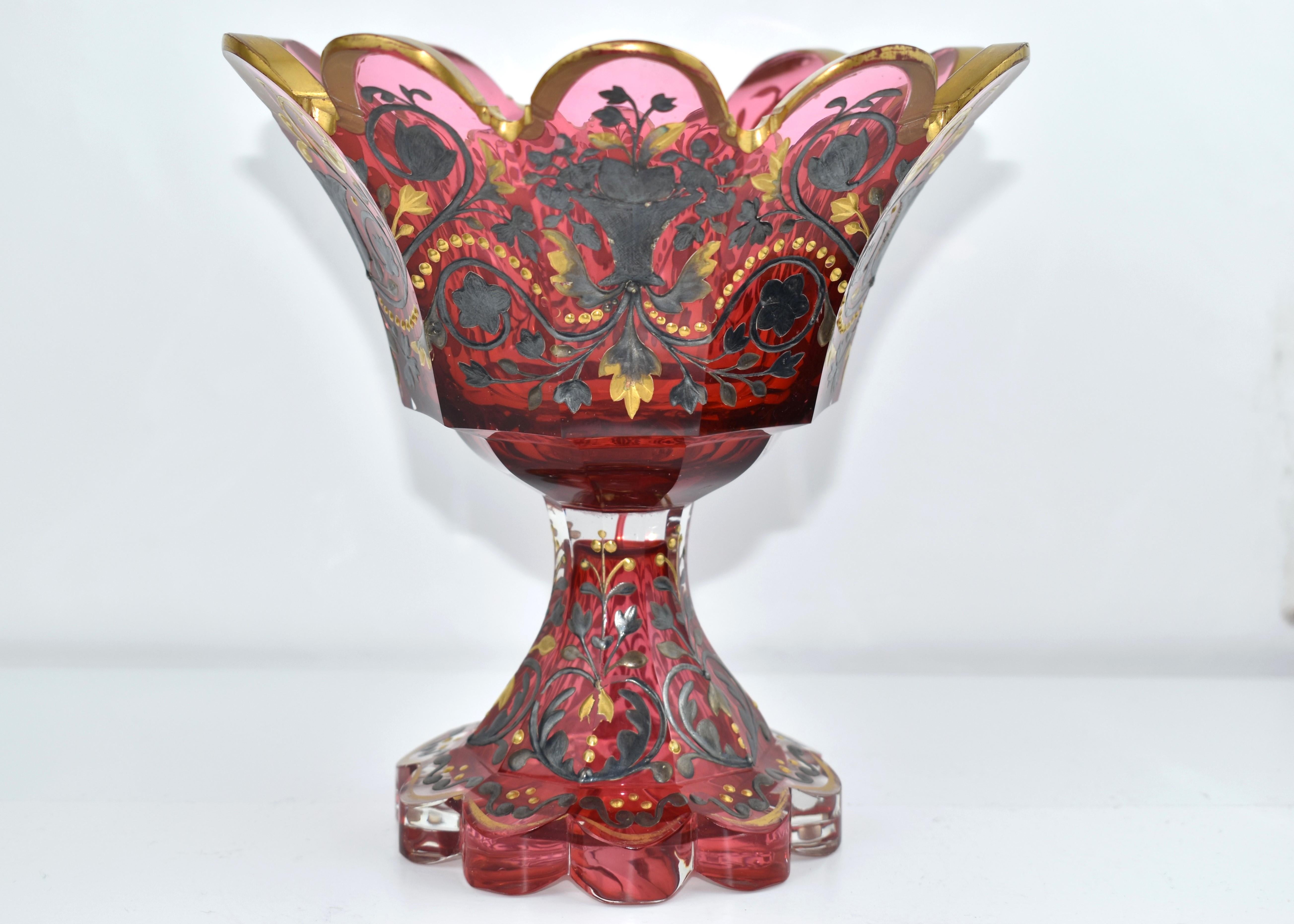 Antique Centerpiece in cranberry glass

stands on a cut glass scalloped foot with flared base at the bottom

richly decorated all around with fine hand-painted gold and silver enamel

fine example of the highest quality Bohemian glass of the 19th