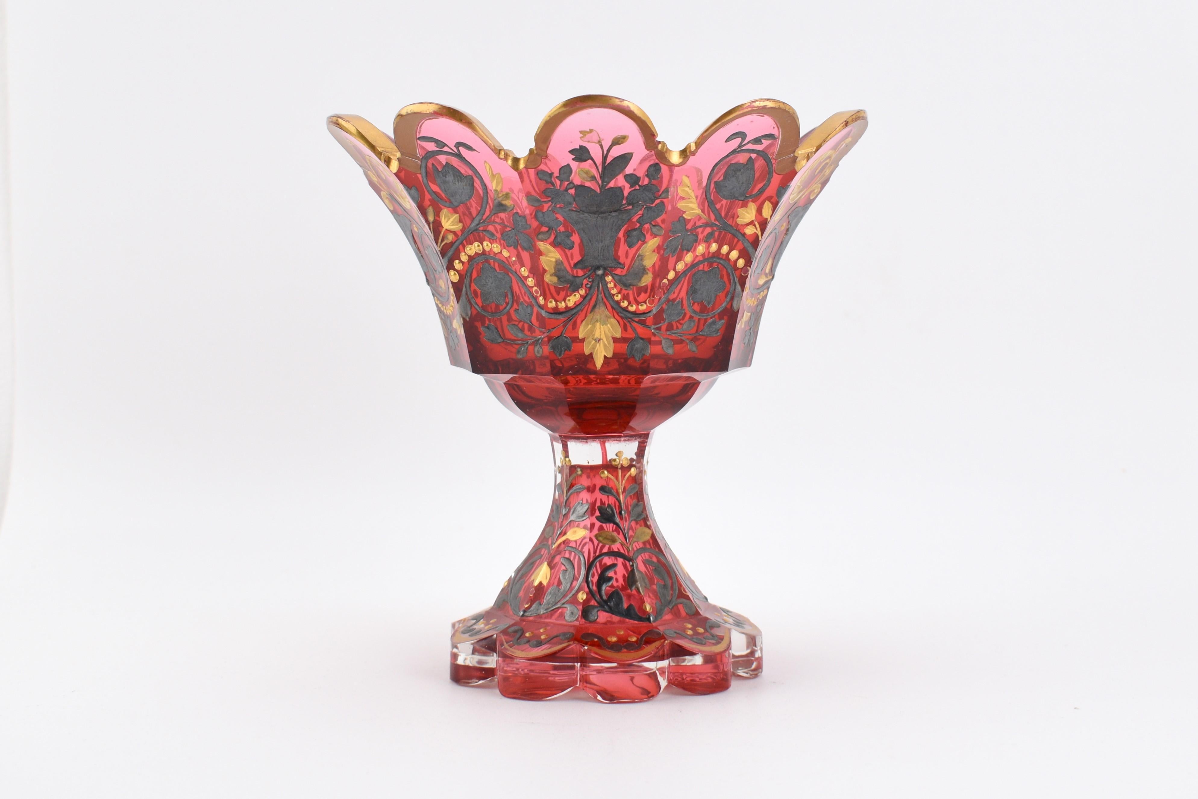 Antiker Tafelaufsatz aus Preiselbeerglas

steht auf einem geschliffenen Glasfuß mit ausgestellter Basis am Boden

rundum reich verziert mit feiner handgemalter Gold- und Silberemaille

schönes Beispiel für die höchste Qualität böhmischen Glases des