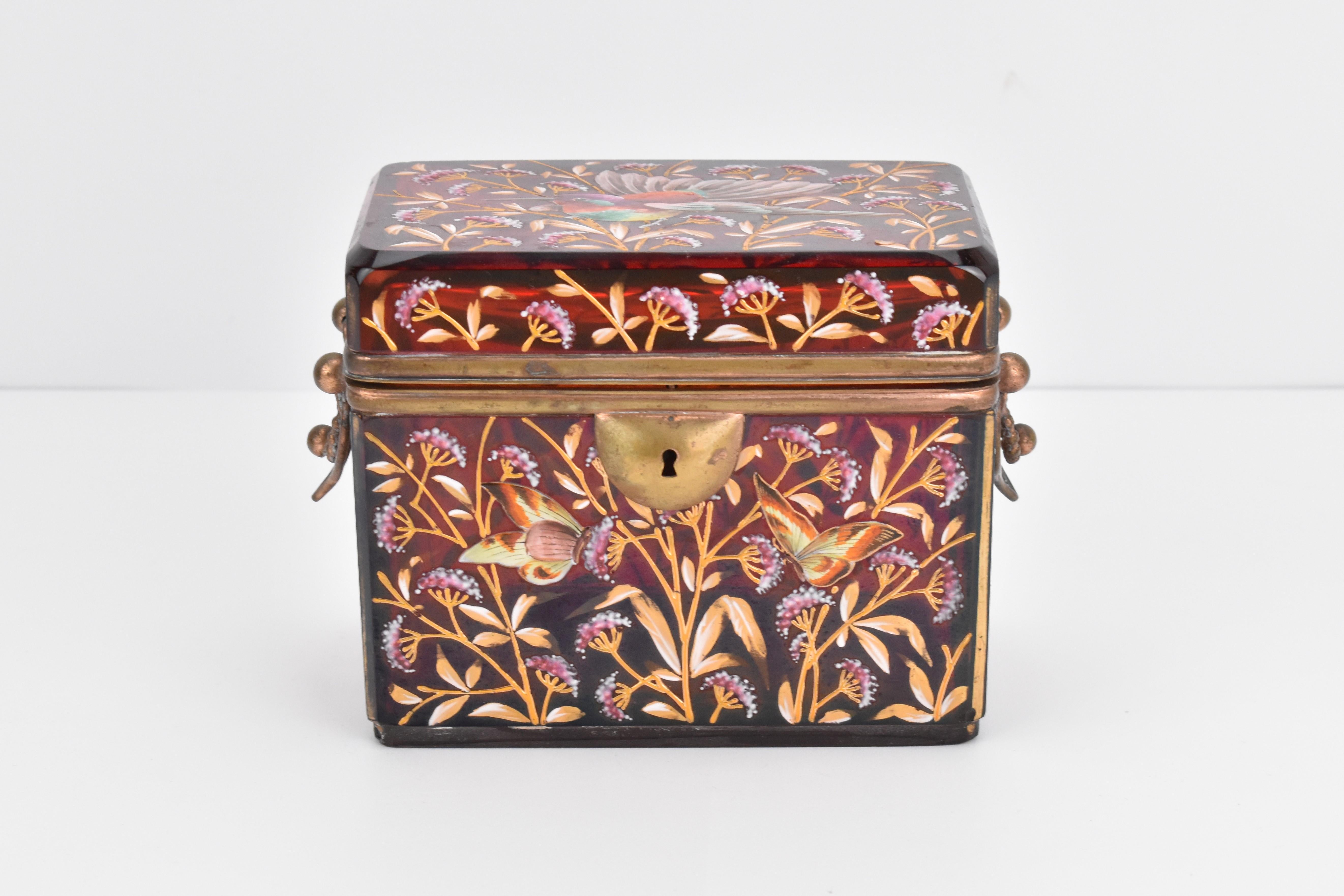 Boîte à bijoux en forme de coffret de Moser avec montures métalliques à charnières

Poignées pivotantes en bronze doré sur les côtés

Généreusement peint à la main sur tout le pourtour avec des décorations en émail coloré représentant des oiseaux,