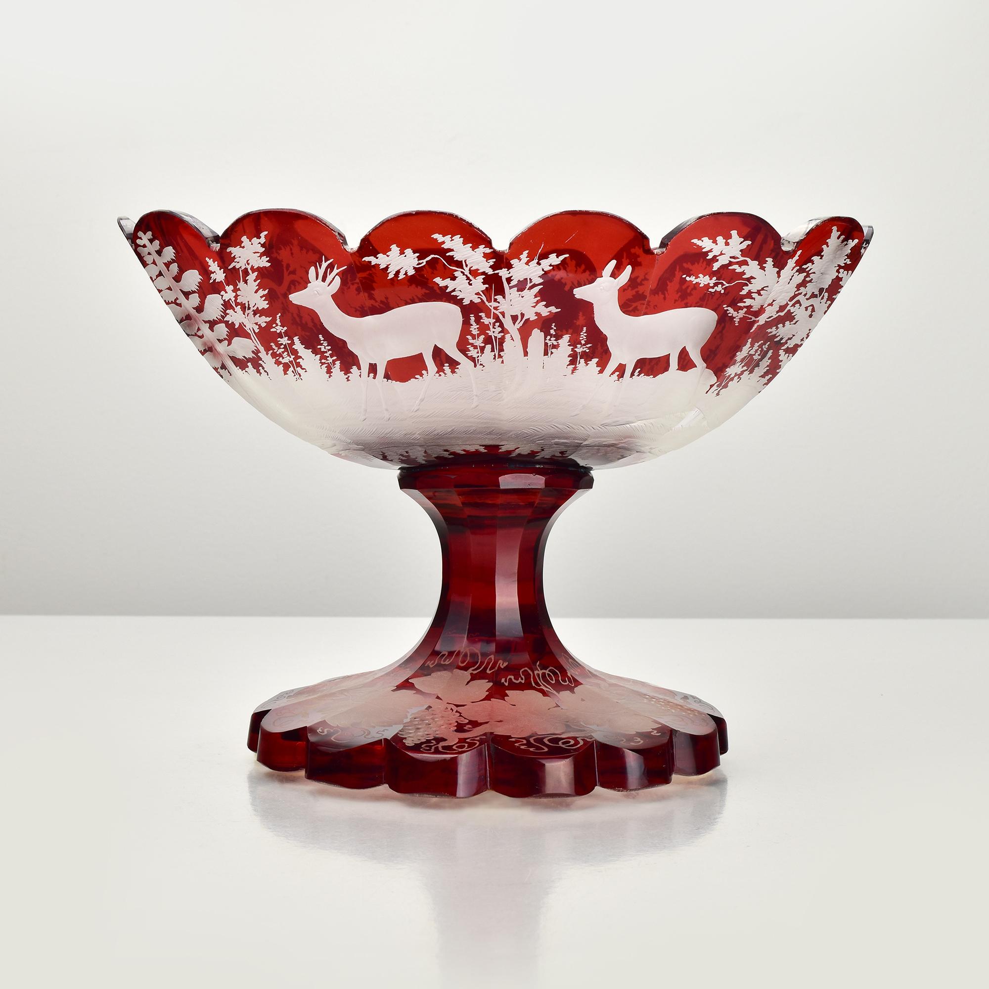 Este exquisito cuenco con pedestal de cristal de Bohemia antiguo muestra una artesanía magistral, con su profundo cristal rubí destellante intrincadamente tallado a rueda y grabado para revelar una encantadora escena de bosque. El cuenco de borde