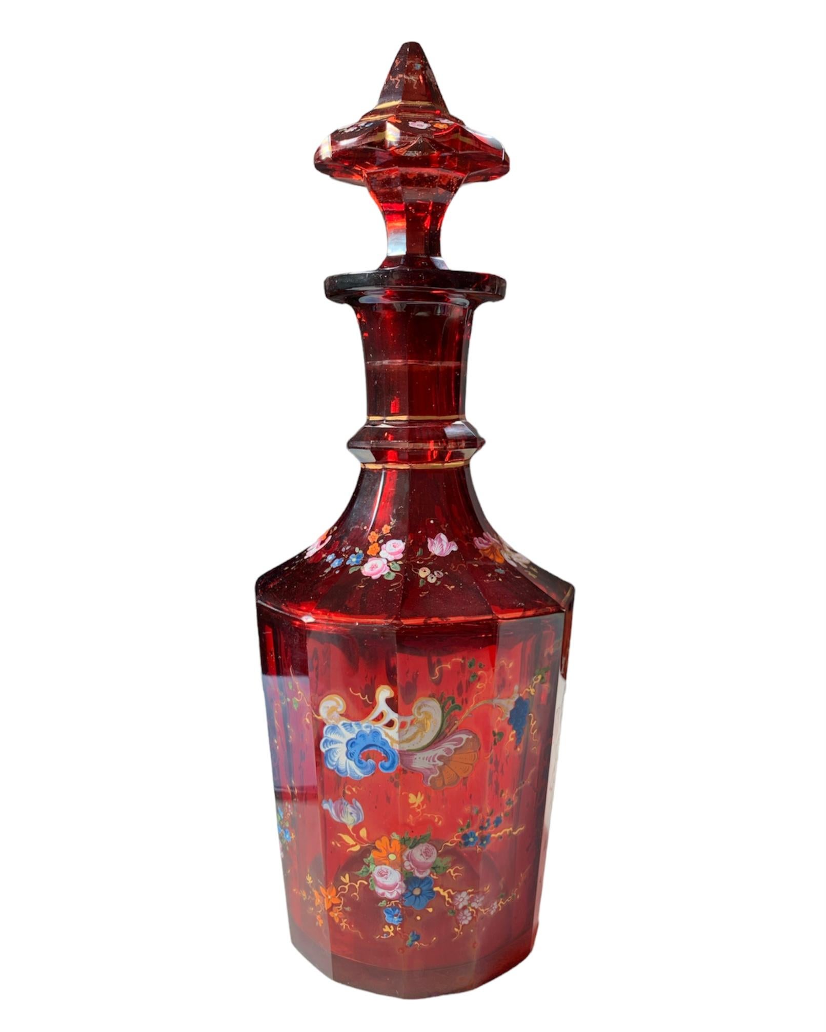 Exceptionally high-quality Bohemian carafe and stopper made of ruby red glass, gilded and decorated with impressive enamel-work, the body cut on 12 side panels, richly decorated all around with colorful gilded enamel featuring scrollwork, vines and