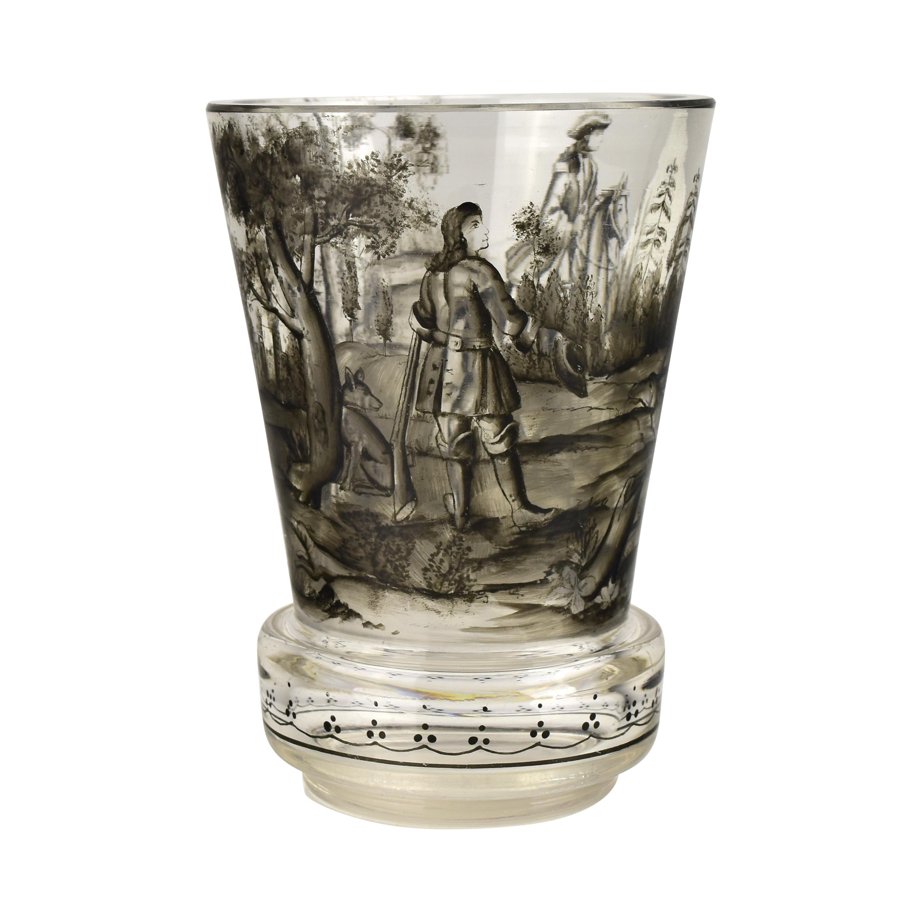 Elegant gobelet ancien en verre de Bohême, finement exécuté en verre clair et décoré selon la technique du Schwarzlot (émail noir). Cette pièce exceptionnelle présente une scène de chasse romantique peinte à la main avec des personnages en tenue