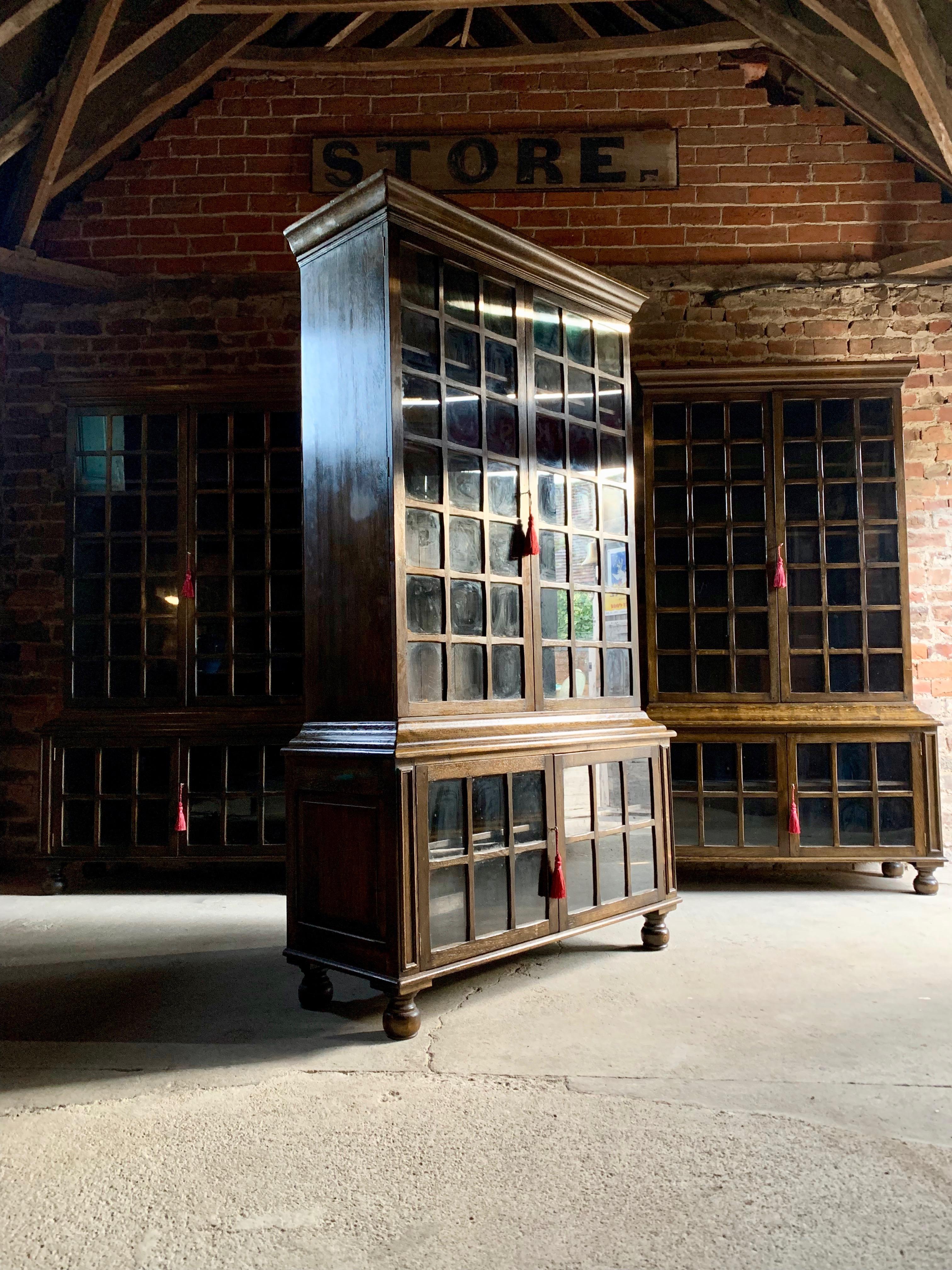 Magnificent and extremely rare set of four early twentieth century ‘Pepys' solid oak double bookcases, circa 1920, having multi-glass paneled twin upper and lower doors and four interior adjustable shelves, raised on turned bun feet, two left