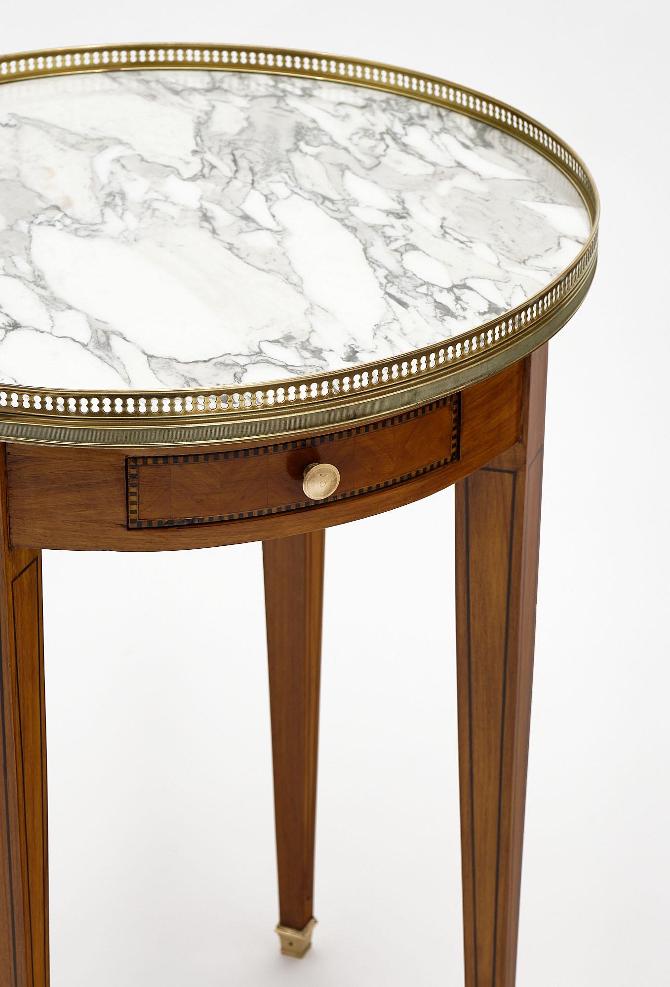 Side table from France in the Louis XVI style. This bouillotte table has chevron marquetry; inlays; and an intact Carrara marble top. There is an opened gilt brass gallery and bronze feet.