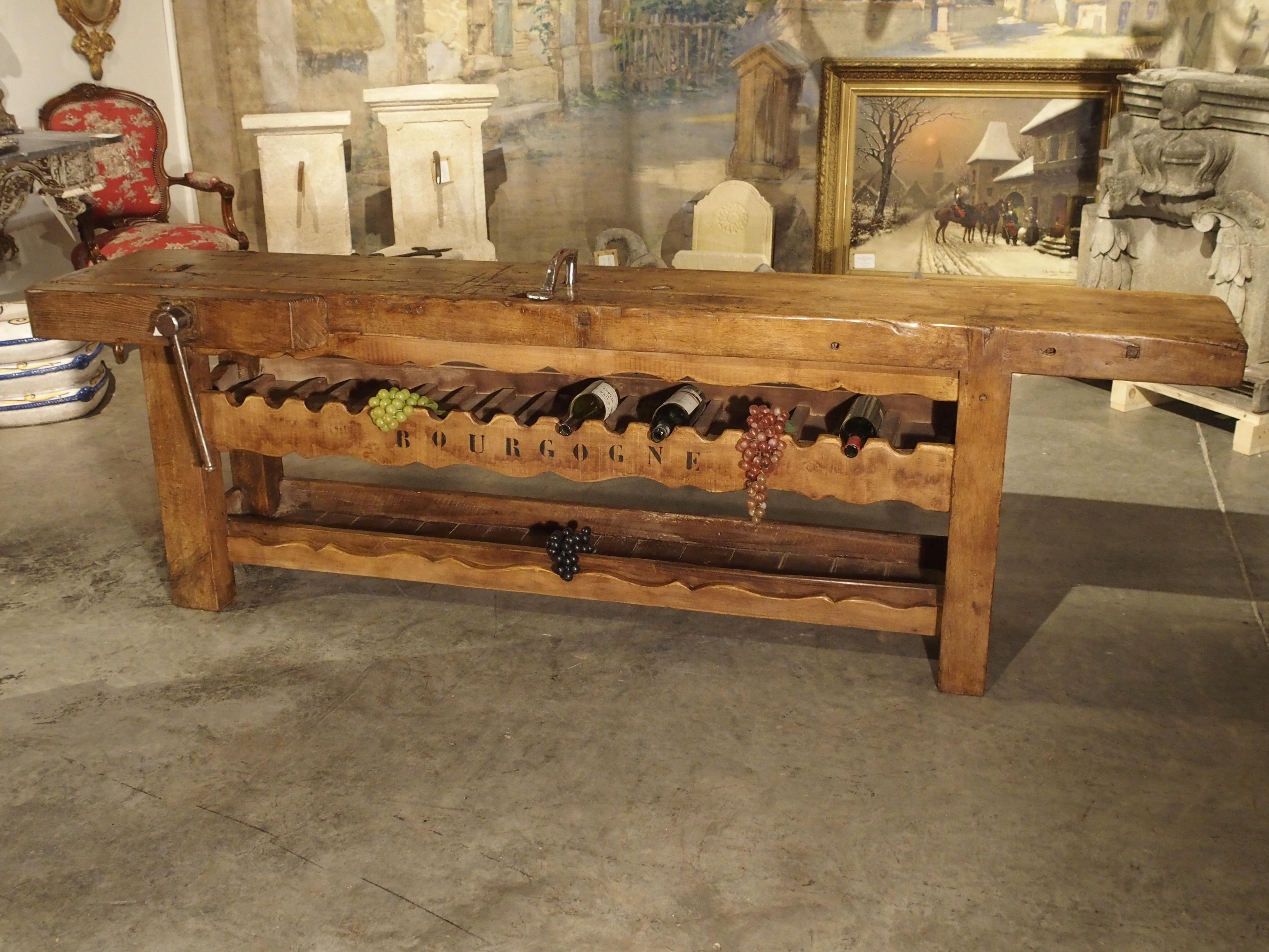 From France, this charming antique workbench has been converted into a large wine bottle holder. The workbench top still has its vise on the left front. There are 16 hand-carved wooden bottle holders on the first rack, with Bourgogne painted in
