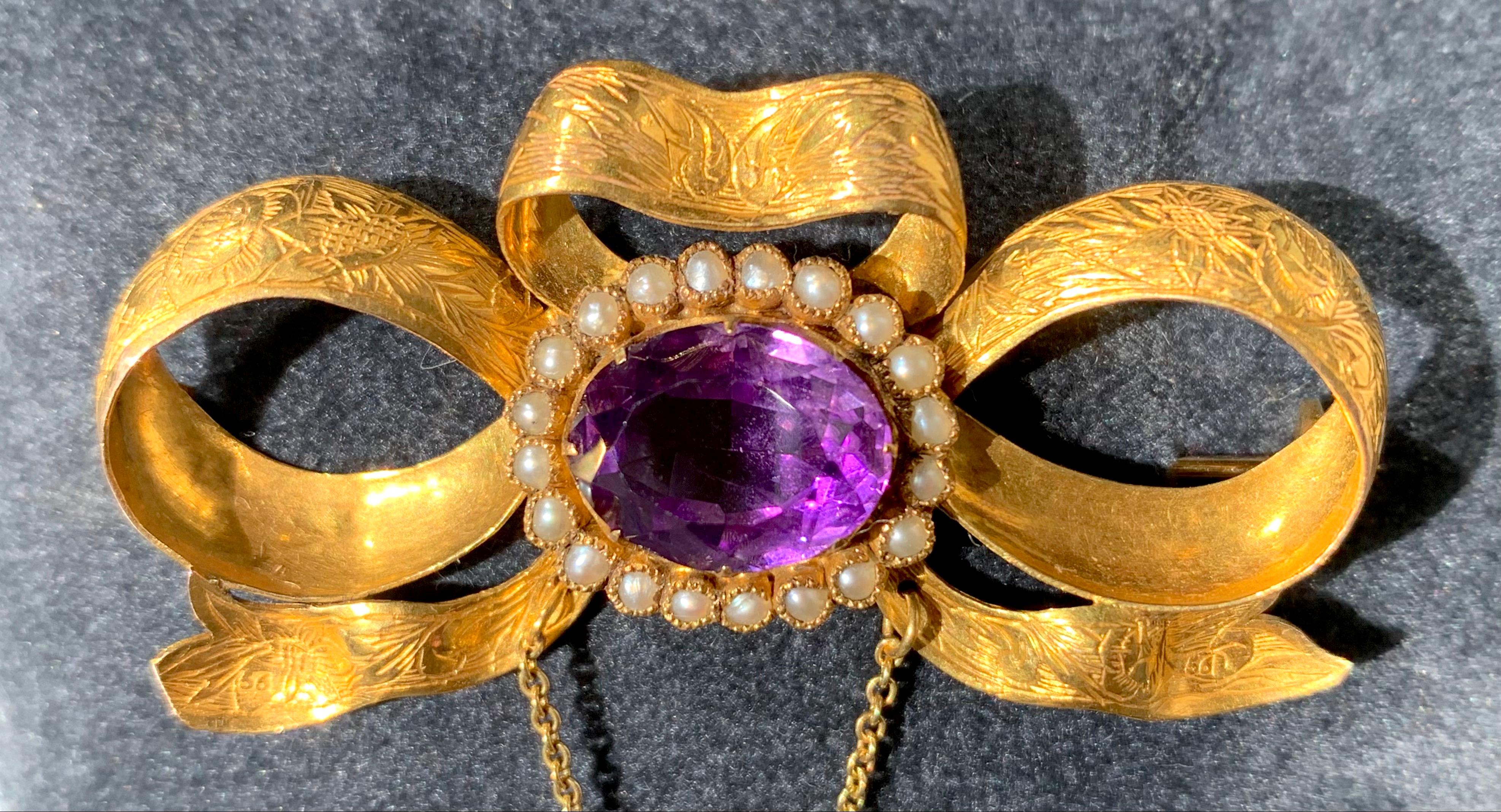 This fine brooch is designed as a bow tied out of an engraved gold ribbon decorated with an oval facetted Russian amethyst mounted in a gold frame set with oriental pearls.
Another amethyst, also mounted with natural oriental pearls, is suspended