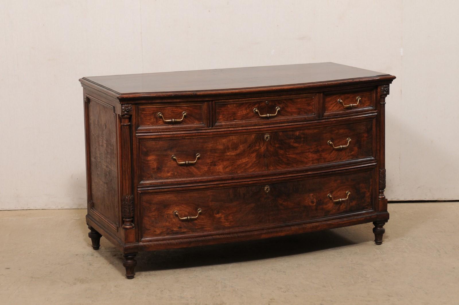 An American bow-front carved wood chest of five drawers from the early 20th century. This antique crotch mahogany wood veneered chest has a beautiful and subtly bowed front, flanked within a pair of round fluted side posts adorn with acanthus leaf
