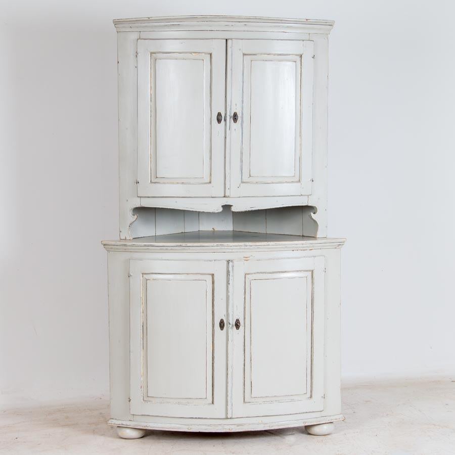 The character of this traditional corner cupboard is revealed in the distressed light gray painted finish which compliments the Swedish styling and brings out the details of the cabinet. This classic painted pine corner cabinet was made in two