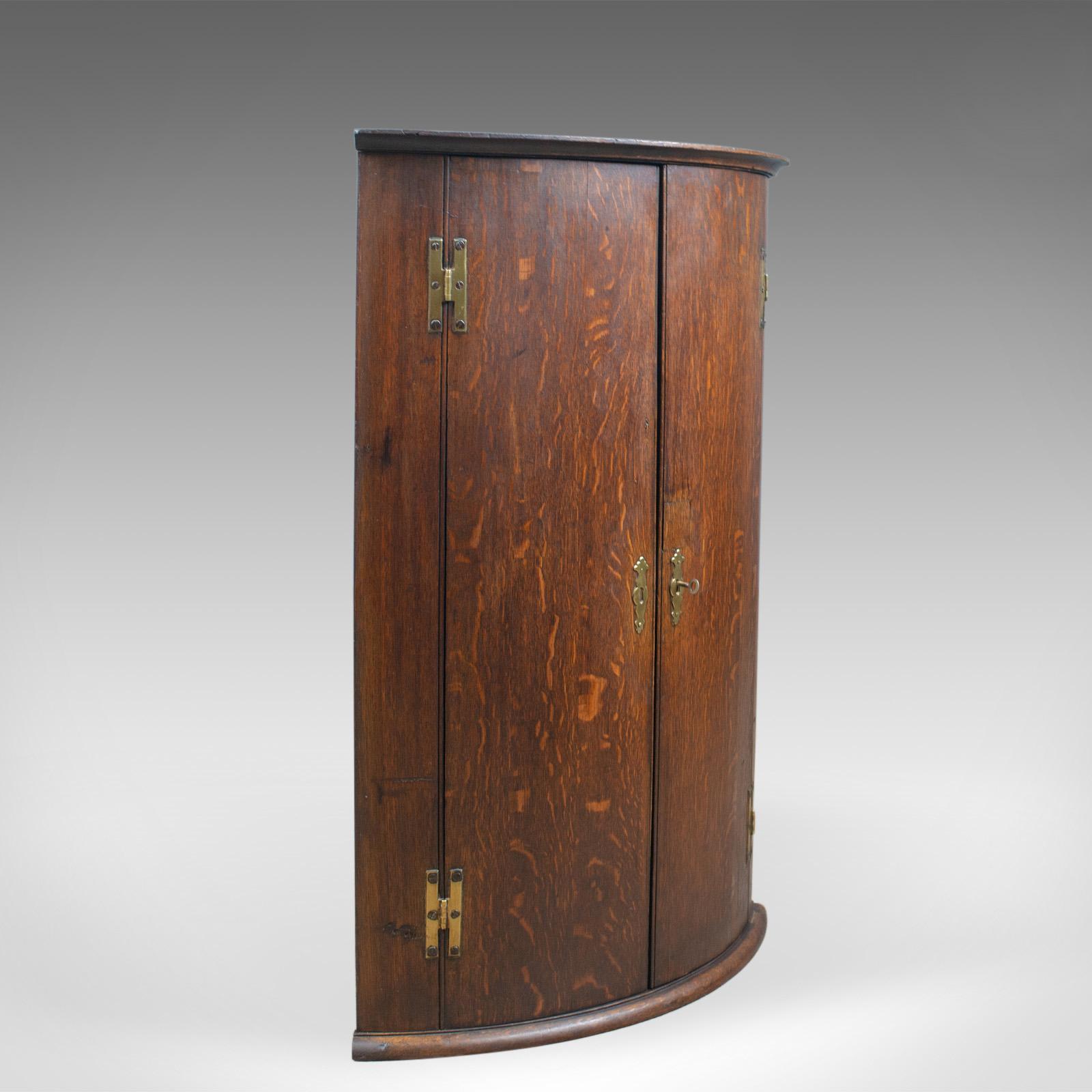 This is an antique bow fronted corner cabinet, an English, oak, Georgian, hanging cupboard dating to the 18th century, circa 1770.

In oak with a very desirable aged tone and fine quality graining
Displaying wisps of medullary rays in through the