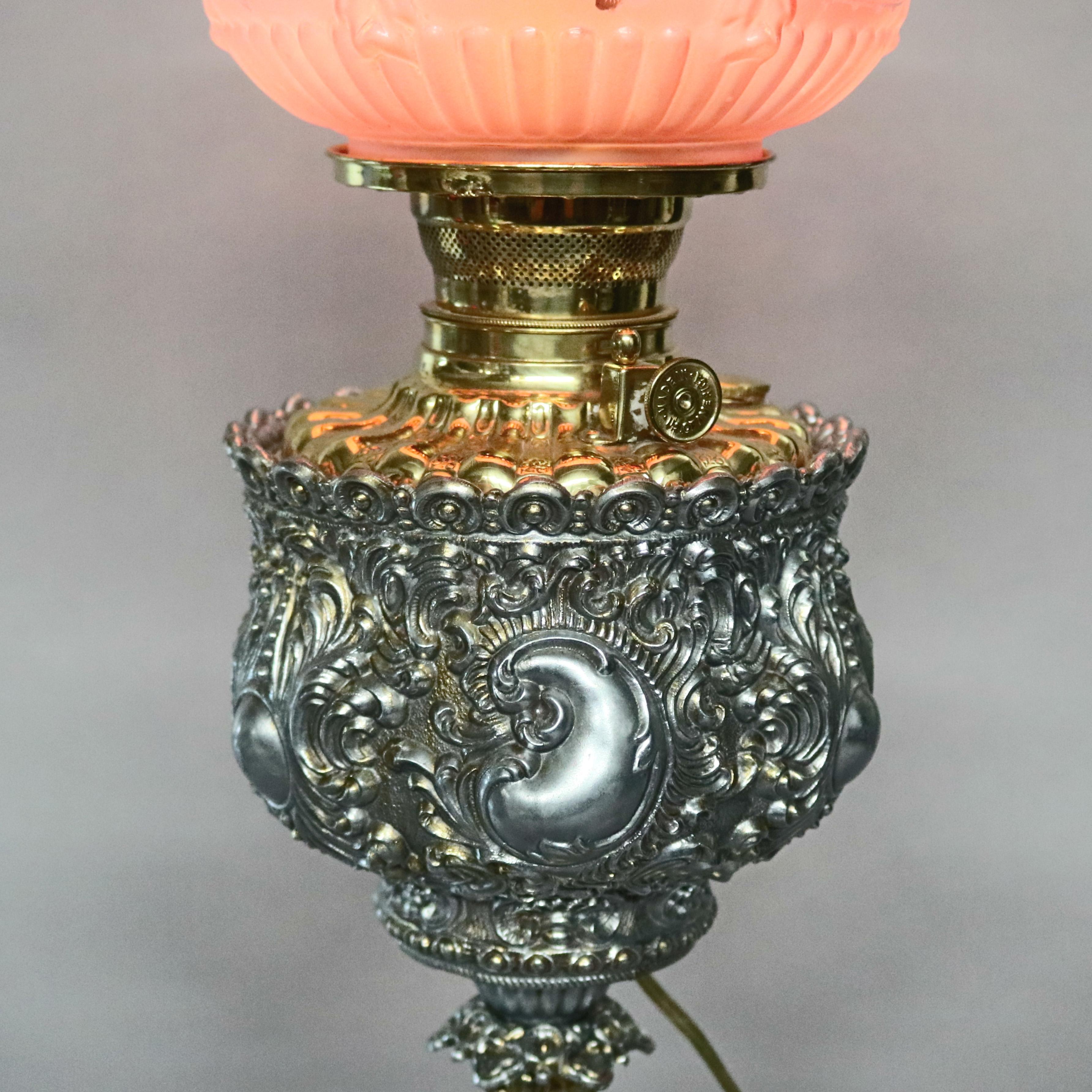 An antique Victorian Bradley and Hubbard School parlor lamp offers two toned gold and silver gilt base in allover foliate relief design supporting blown out cranberry satin glass shade and raised on four scroll form feet, electrified, circa