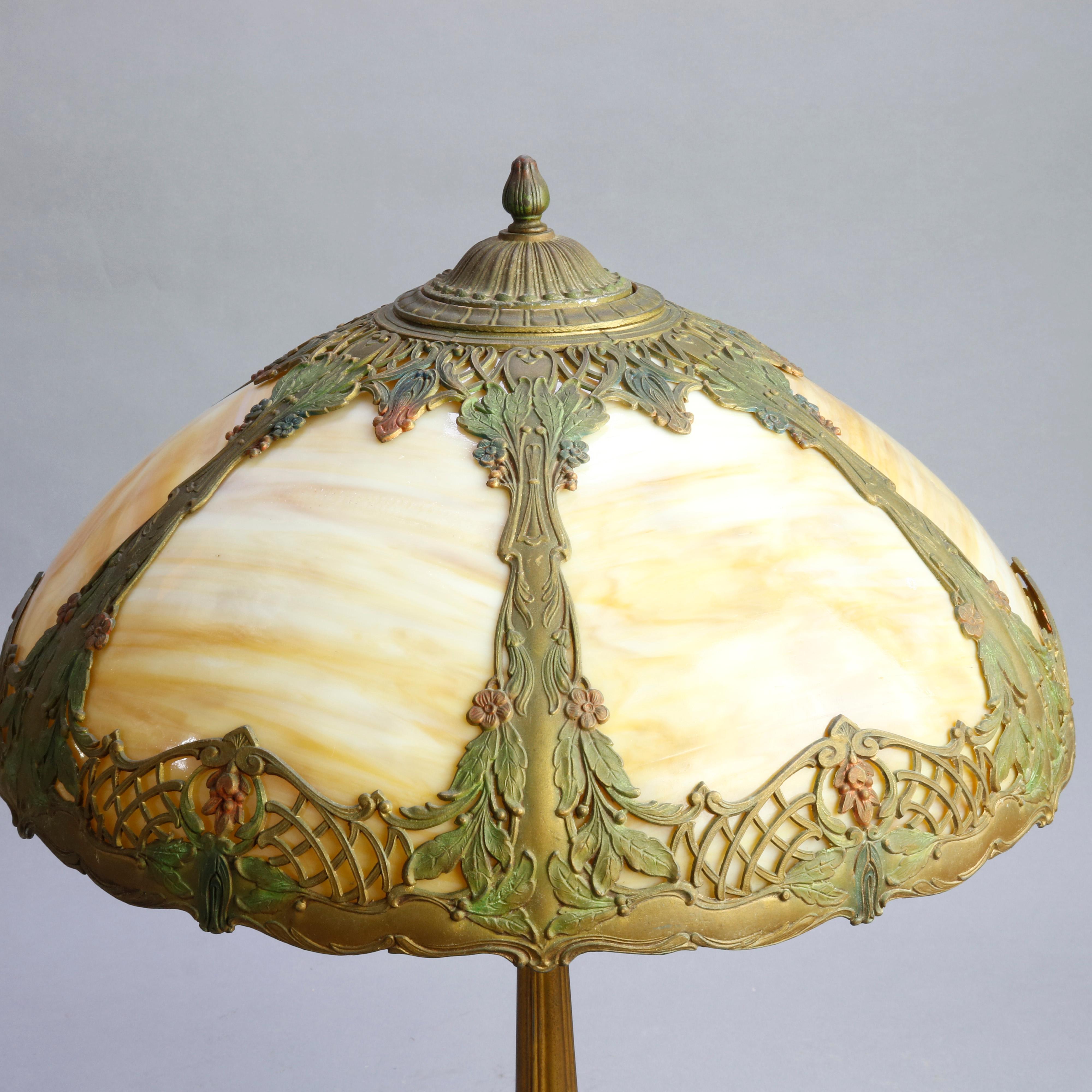 An antique table lamp in the manner of Bradley and Hubbard offers polychromed filigree cast shade having foliate elements and housing bent slag glass panels, surmounting double socket base, professionally rewired and new sockets, circa