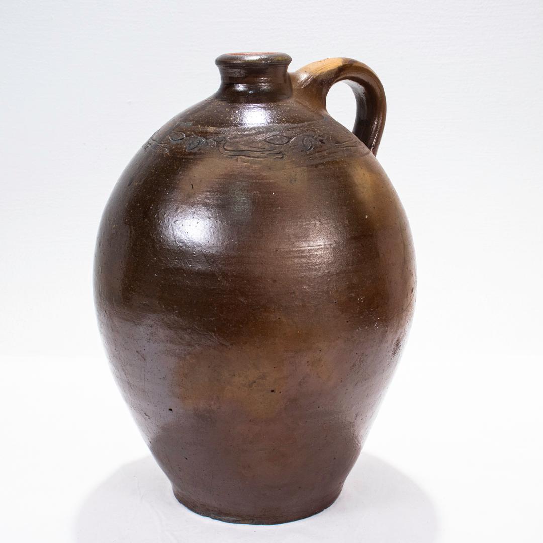 A fine antique American stoneware jug.

Attributed to the Branch Green Pottery in Philadelphia, PA.

Of ovoid form with an applied handle and a tooled spout.

Decorated to the shoulder with a coggled design of a bird with a leaf (or branch) in its