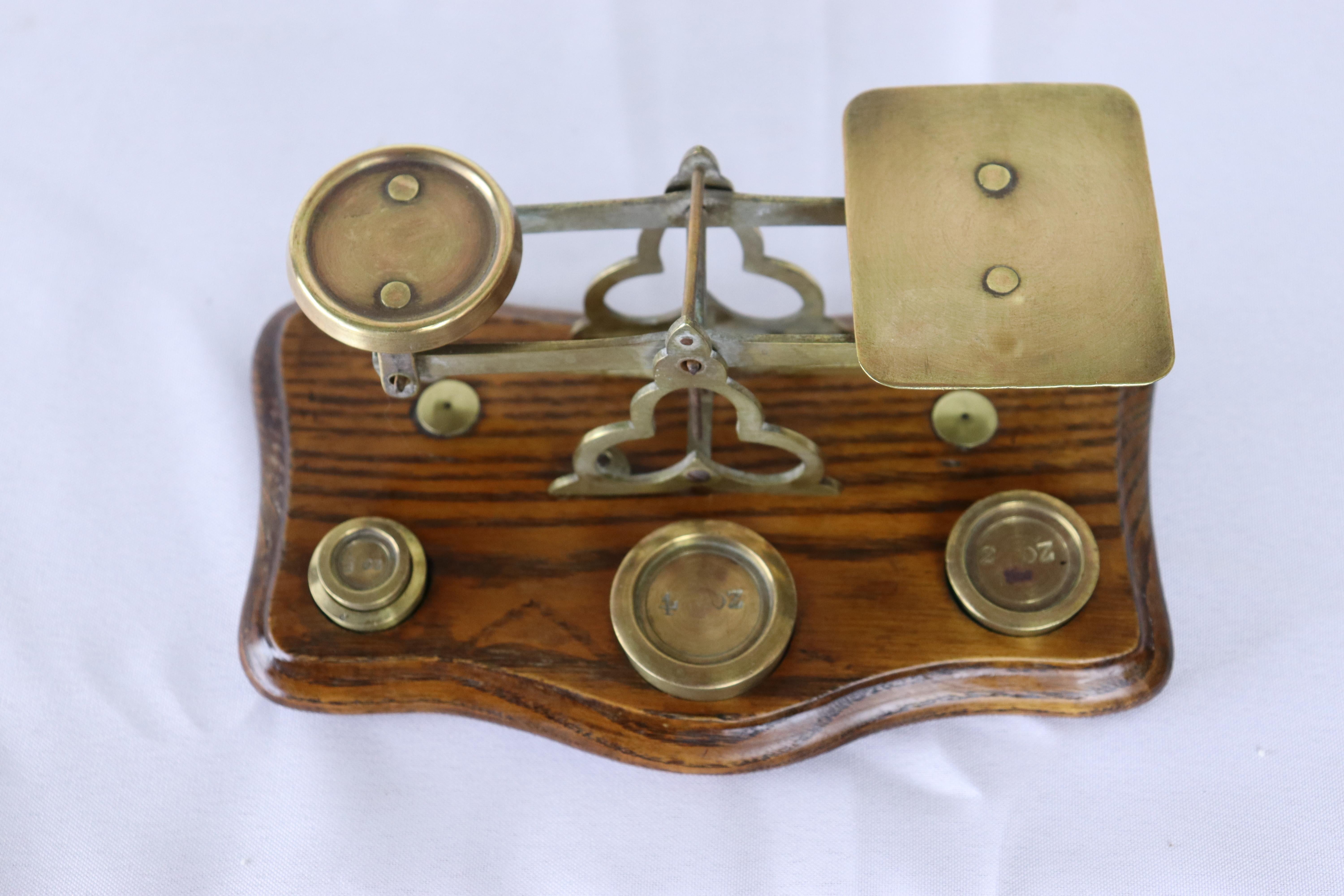 A small antique brass and wood English postal scale. It stands on an oak base with serpentine edge. There are 4 weights which measure 4 oz,  2oz, 1 oz and 1/2 oz. 