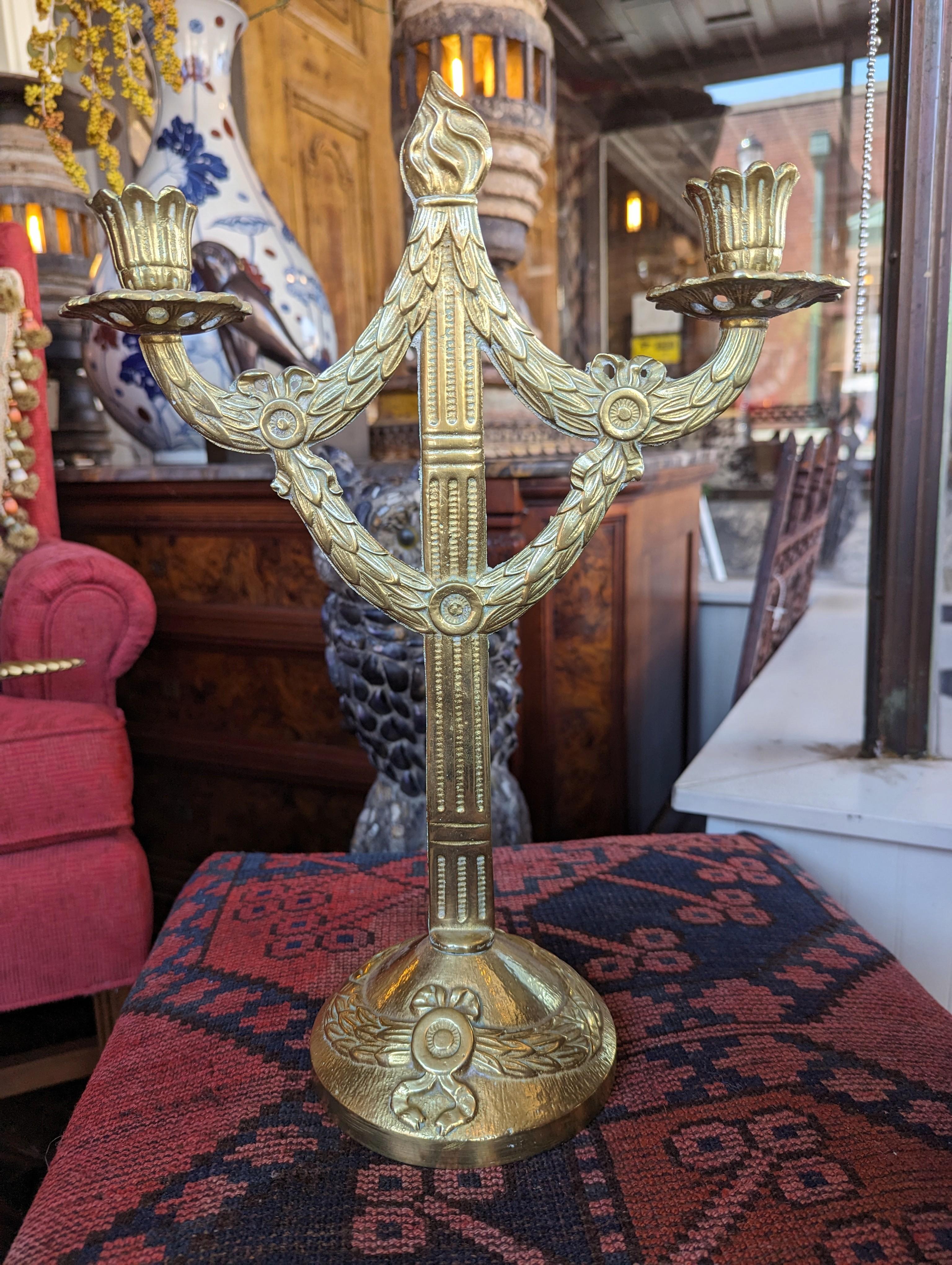 Elegant and detailed antique brass candelabra with a classical ribbon and wreath motif. Fits two candles and has original patina due to age, measures 15.5 inches in height by 11 inches in width.